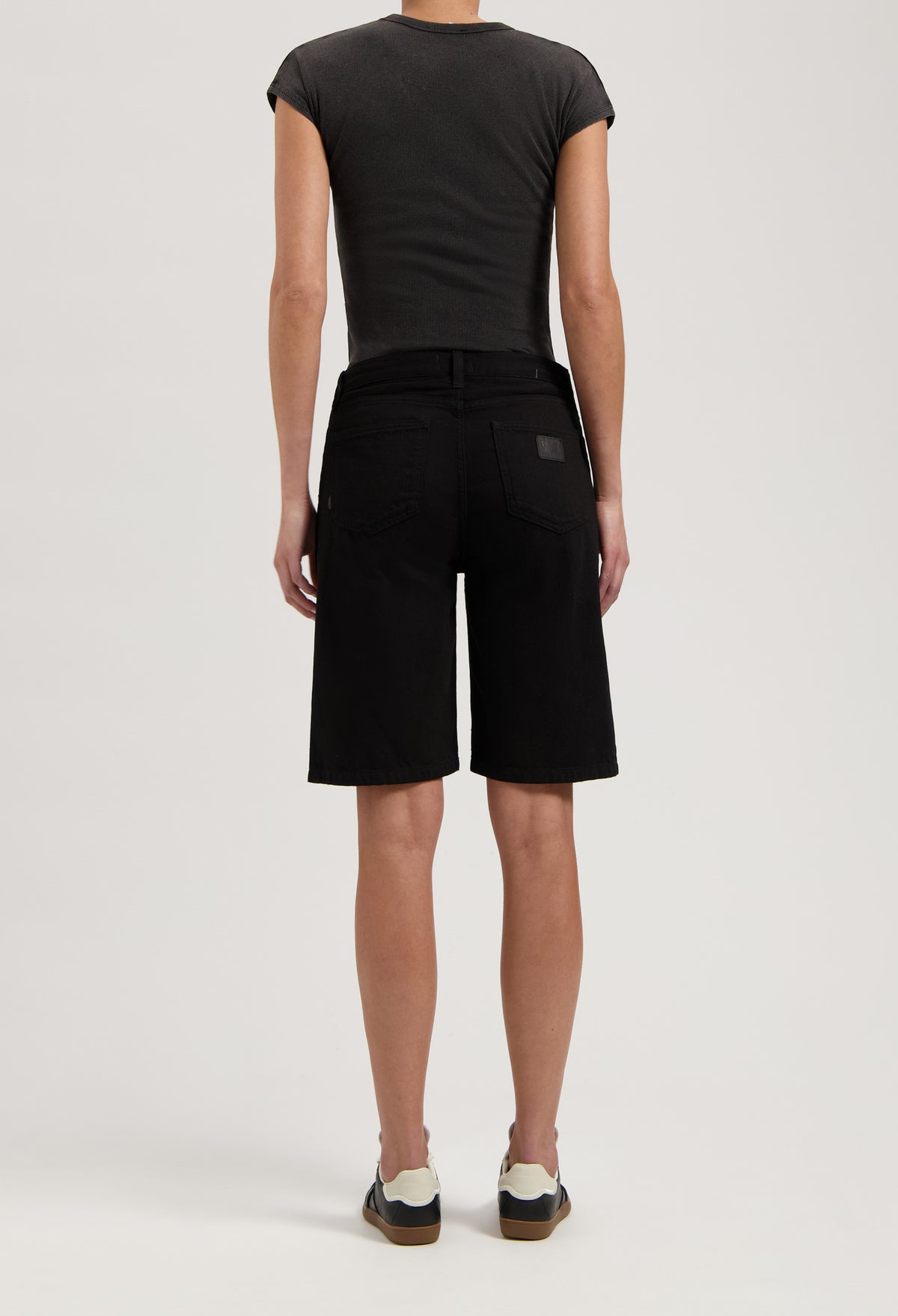Black denim shorts styled with a fitted dark gray top and casual sneakers, highlighting a modern summer outfit.