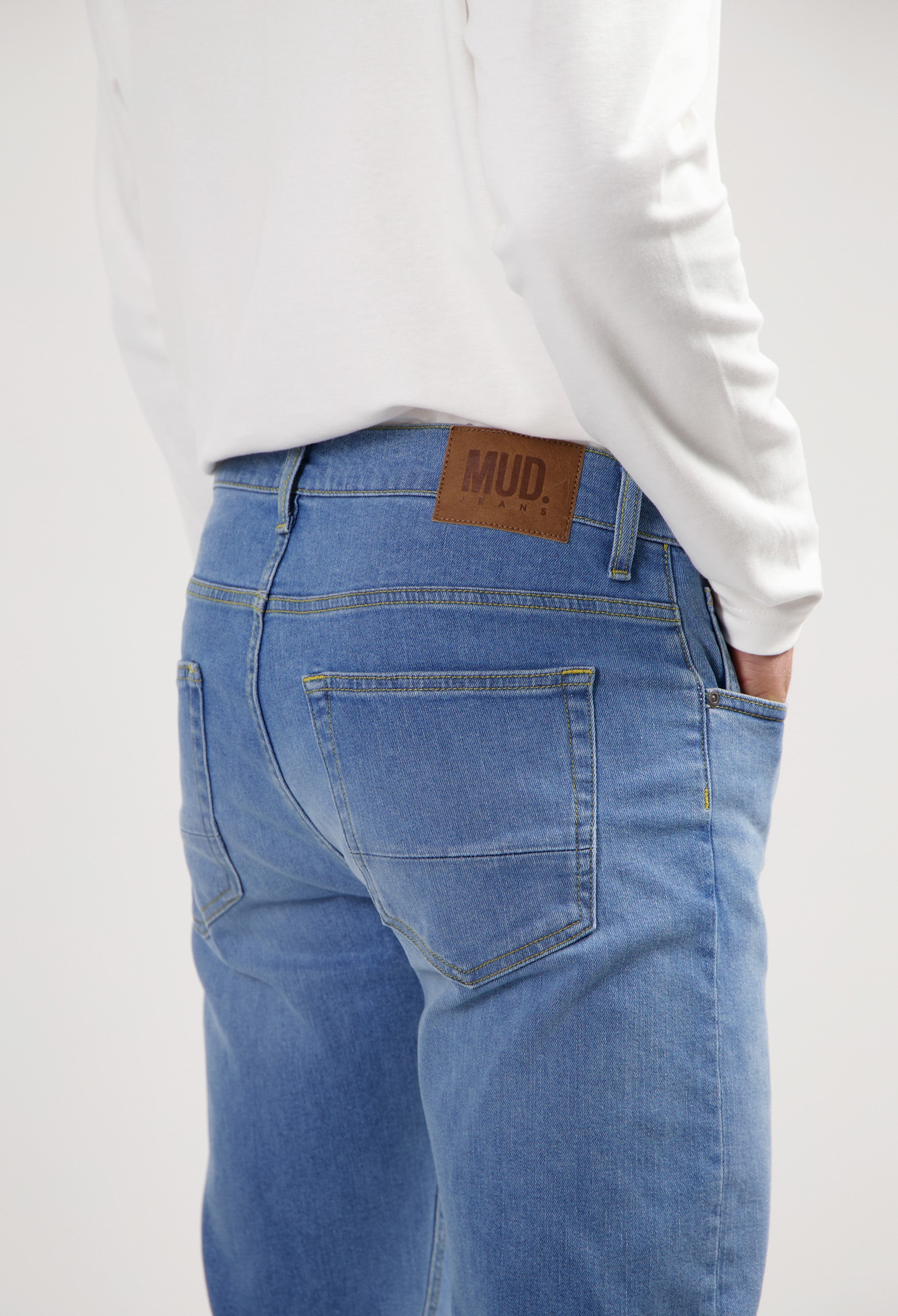 Sustainable MUD Jeans in light blue denim, crafted from organic cotton, paired with a casual gray shirt and white sneakers.