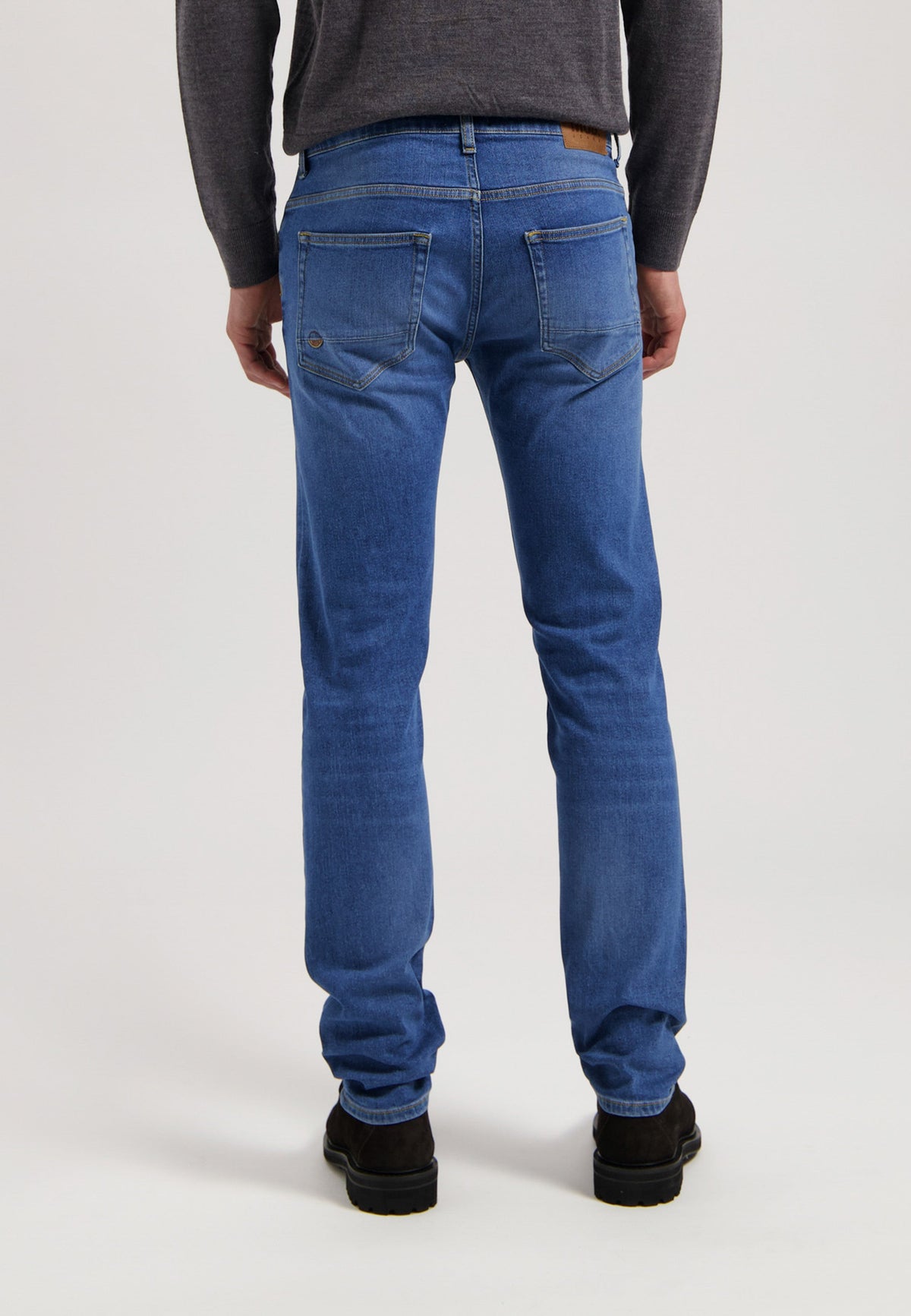 Sustainable MUD Jeans in deep indigo blue, crafted from eco-friendly materials, styled with a gray T-shirt and white sneakers.