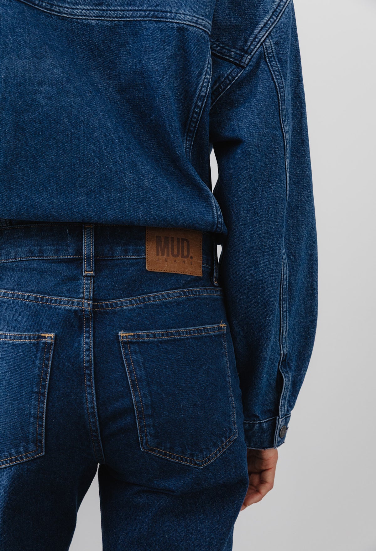Back view of recycled dark blue denim jacket and jeans set, featuring MUD Jeans logo on leather patch above pocket.