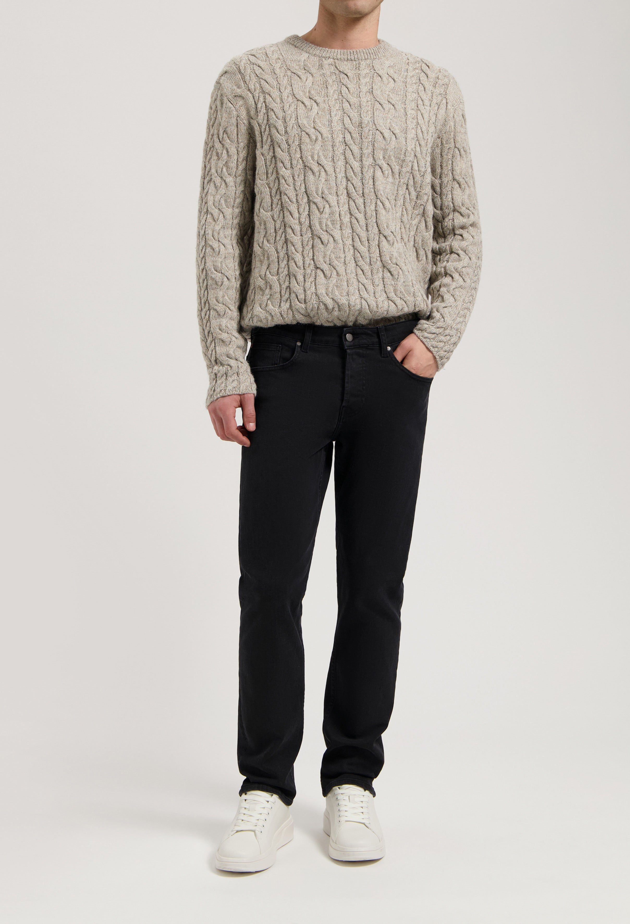 Sustainable MUD Jeans in black denim, showcasing ethical fashion with a classic fit, paired with a beige cable-knit sweater.