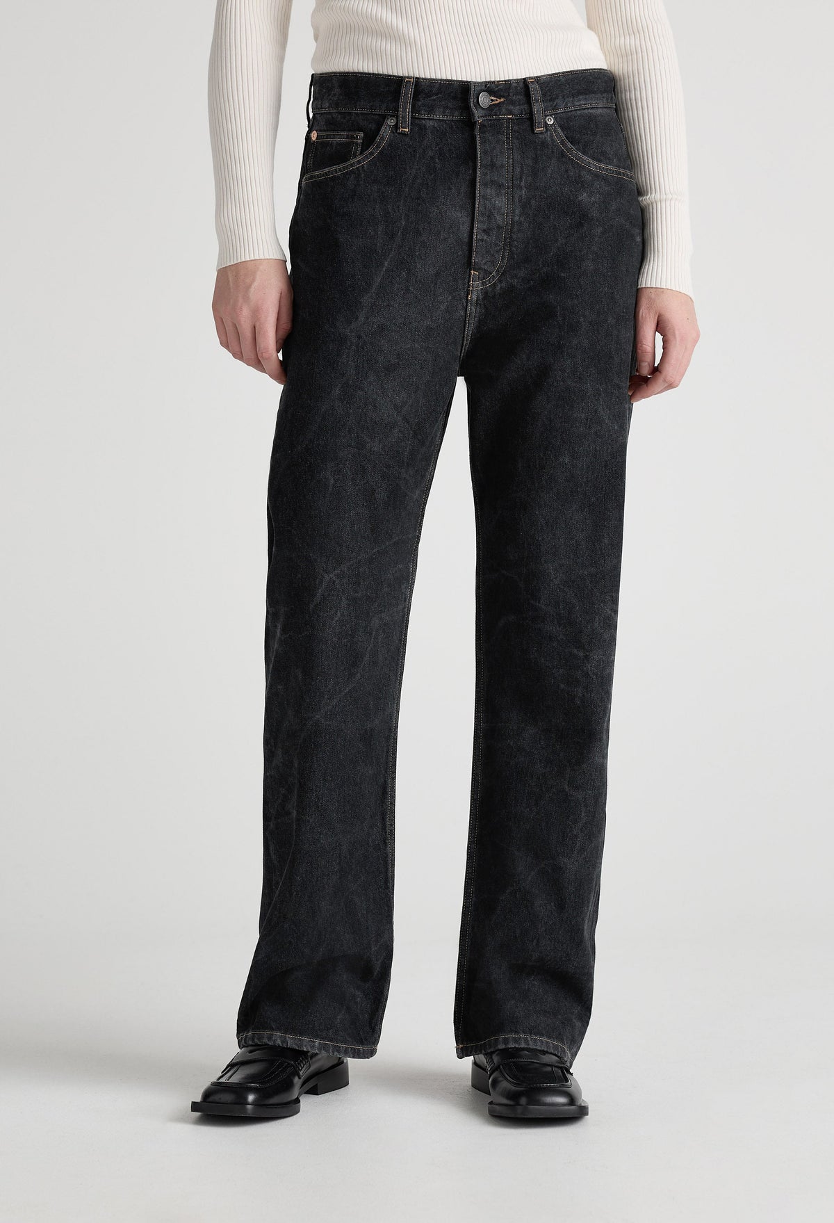 A model wearing loose-fitting black denim jeans with a ribbed, white long-sleeve top and black leather shoes.