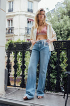 Casual summer outfit featuring wide-leg light blue jeans, paired with a red and white striped bralette and a beige shirt.