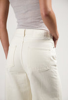 MUD Jeans in off-white denim, showcasing high-waisted design, rear pockets, and a soft texture worn with a gray fitted top.
