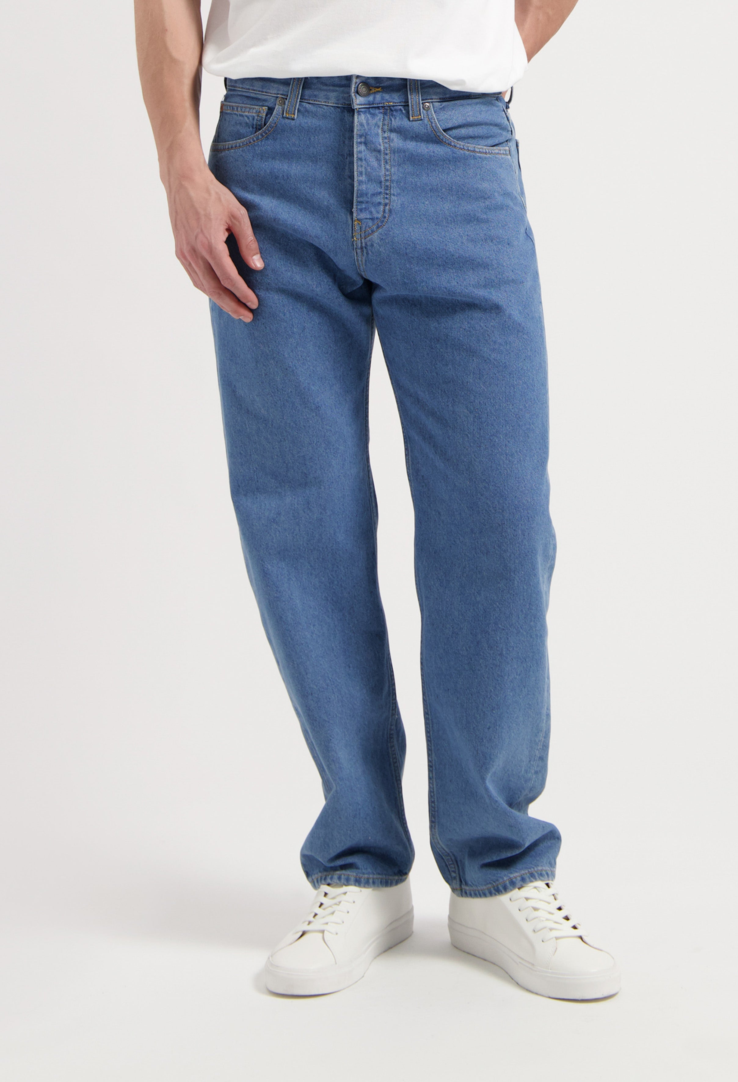 Sustainable MUD Jeans in classic blue denim, featuring an ethical design, paired with black shoes and a charcoal sweater.