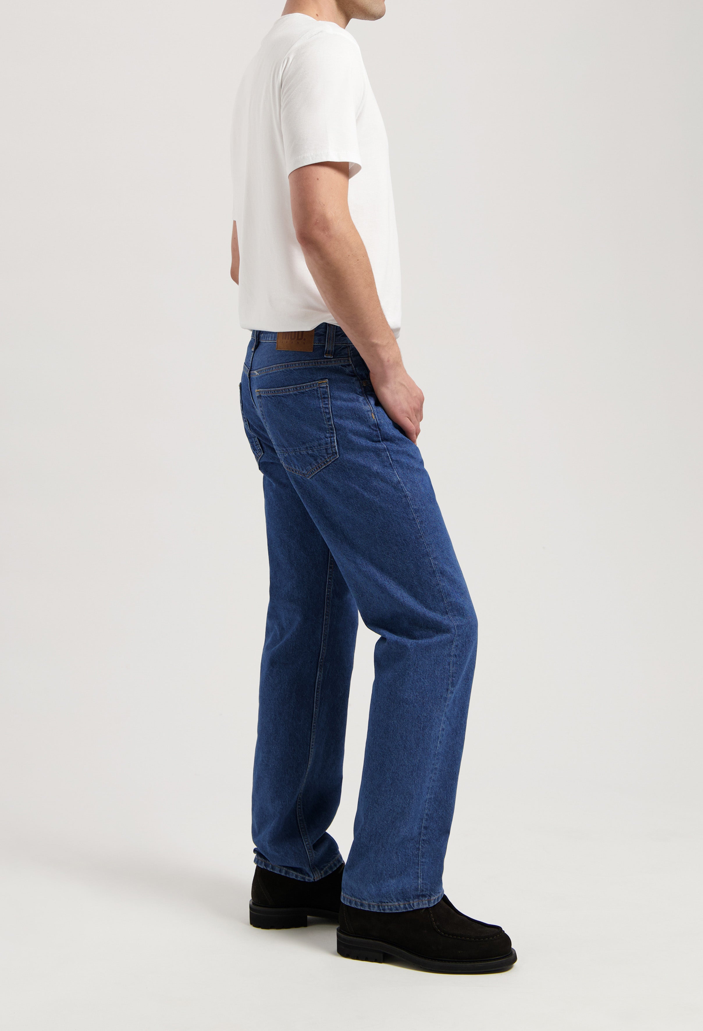 Sustainable MUD Jeans in gray denim, crafted from organic cotton, paired with a white T-shirt and black shoes.