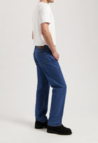 Sustainable MUD Jeans in gray denim, crafted from organic cotton, paired with a white T-shirt and black shoes.