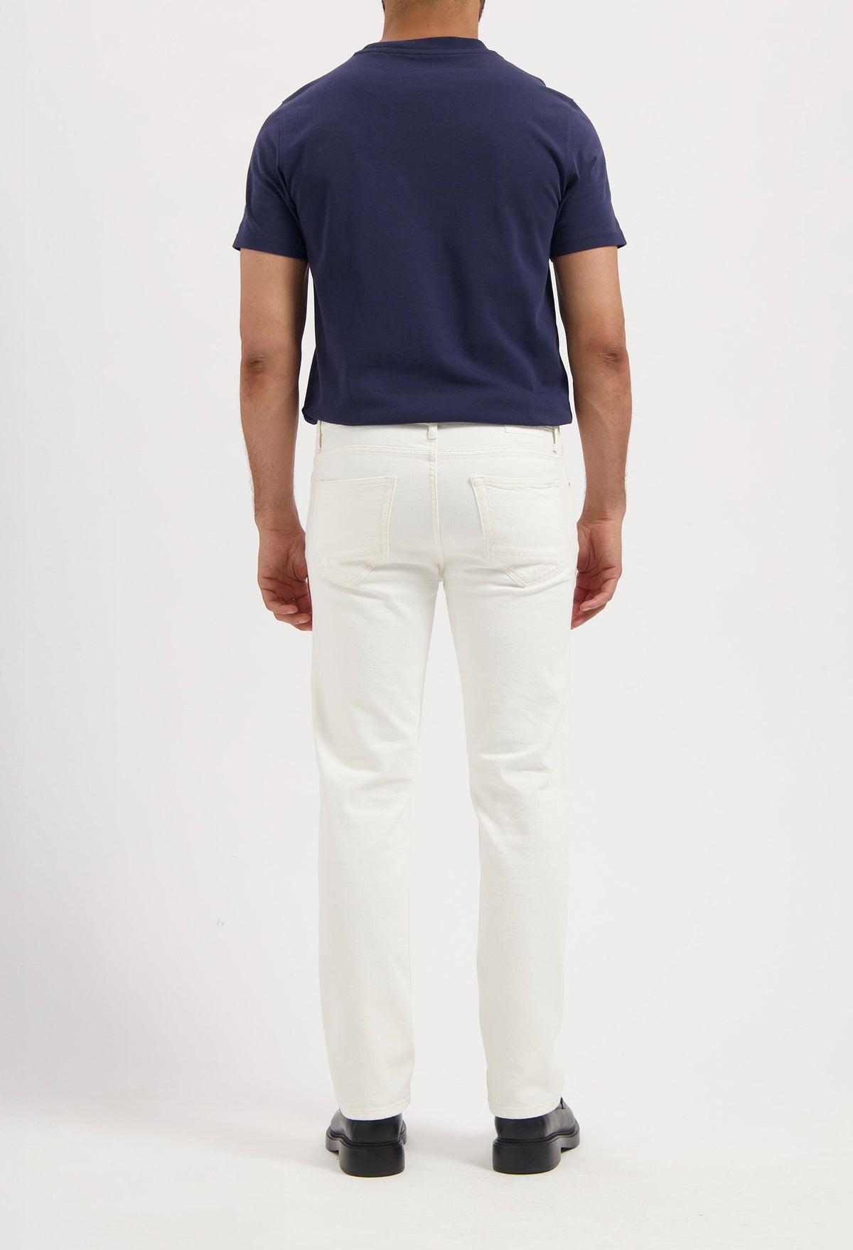 Sustainable MUD Jeans in dark indigo denim, paired with white sneakers, embodying ethical fashion.