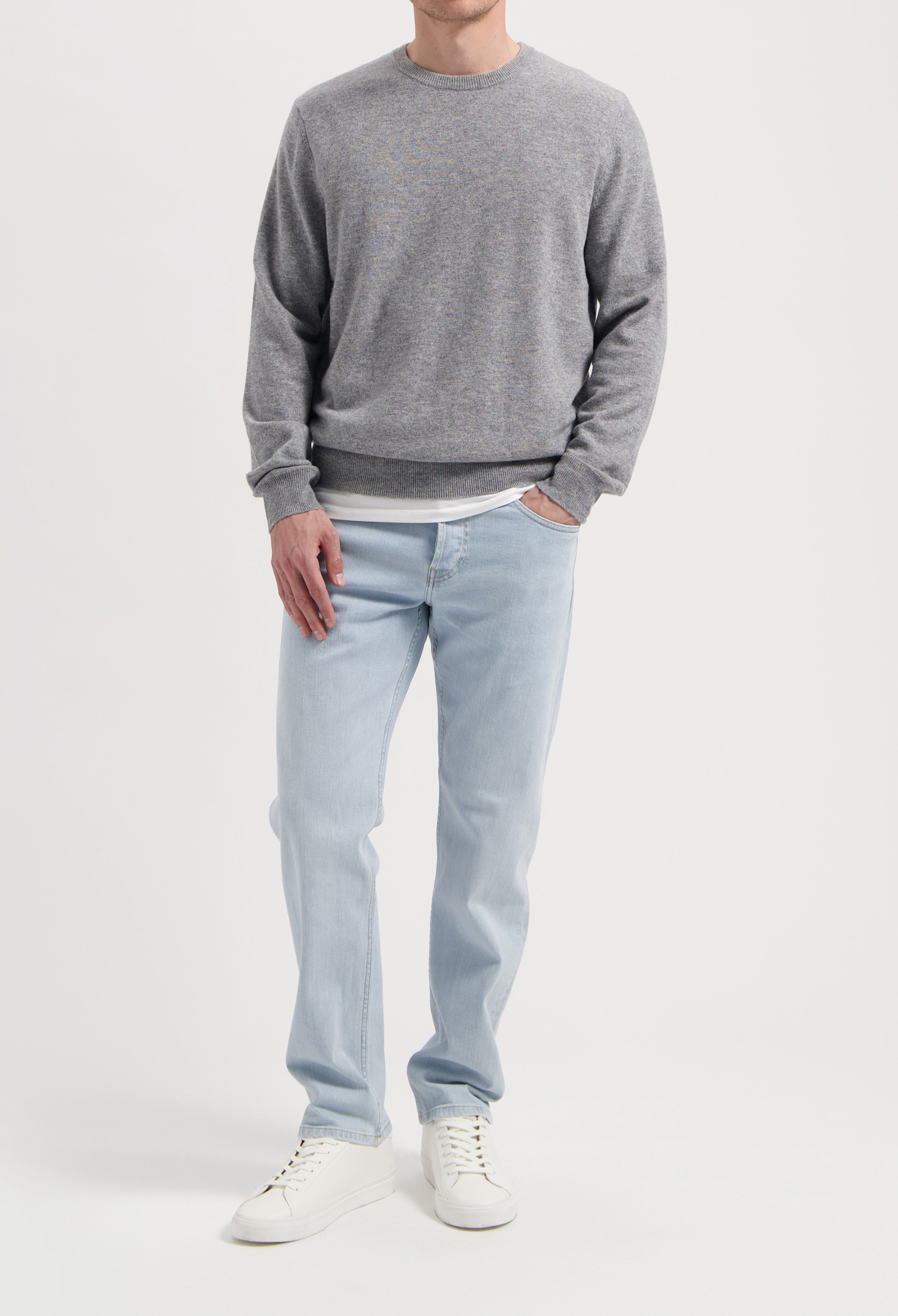 Sustainable MUD Jeans in gray denim, featuring an ethical, classic fit, paired with a black sweater and sneakers.