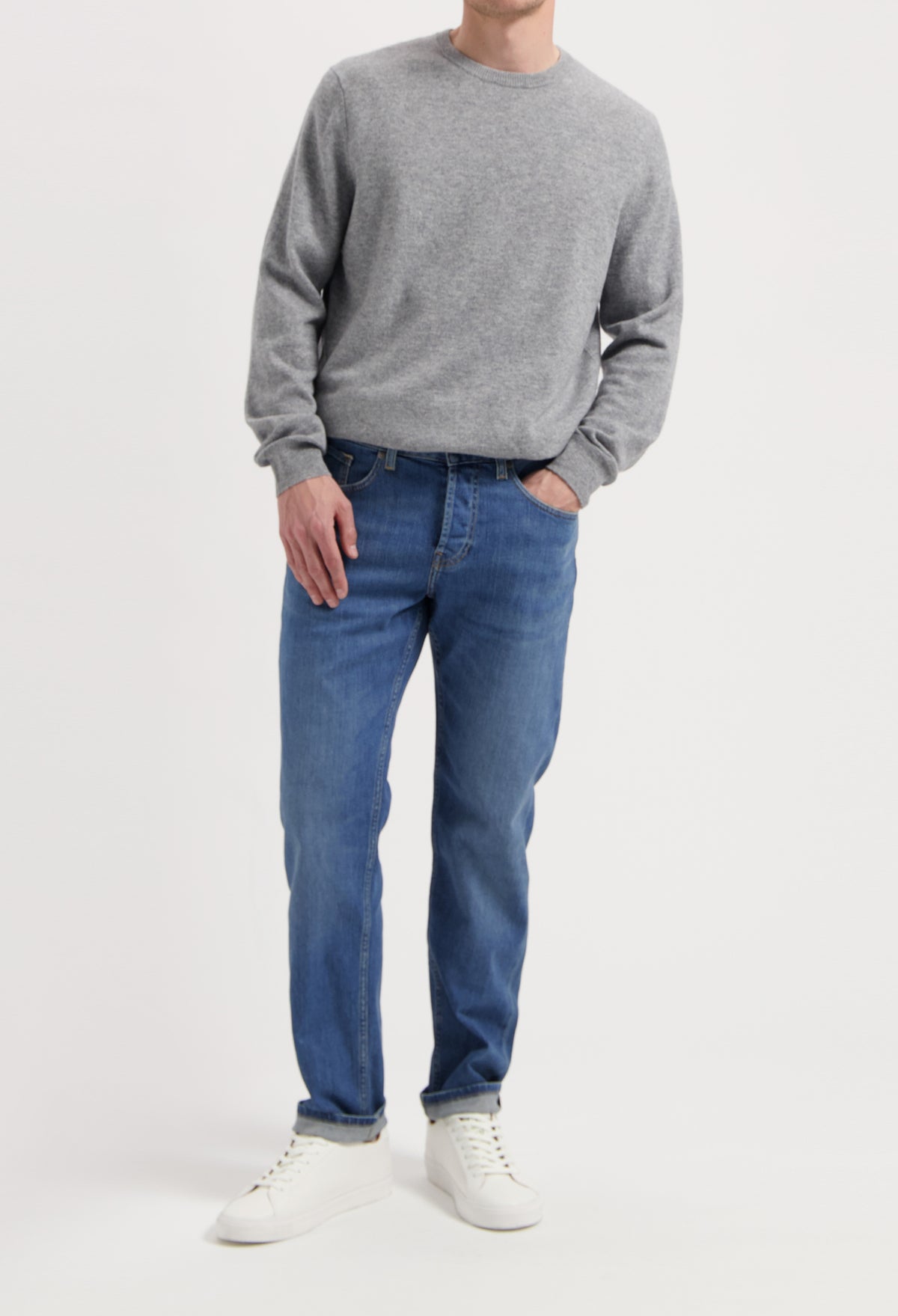 Sustainable MUD Jeans in medium blue denim, styled with a dark blue jacket, emphasizing ethical fashion choices.