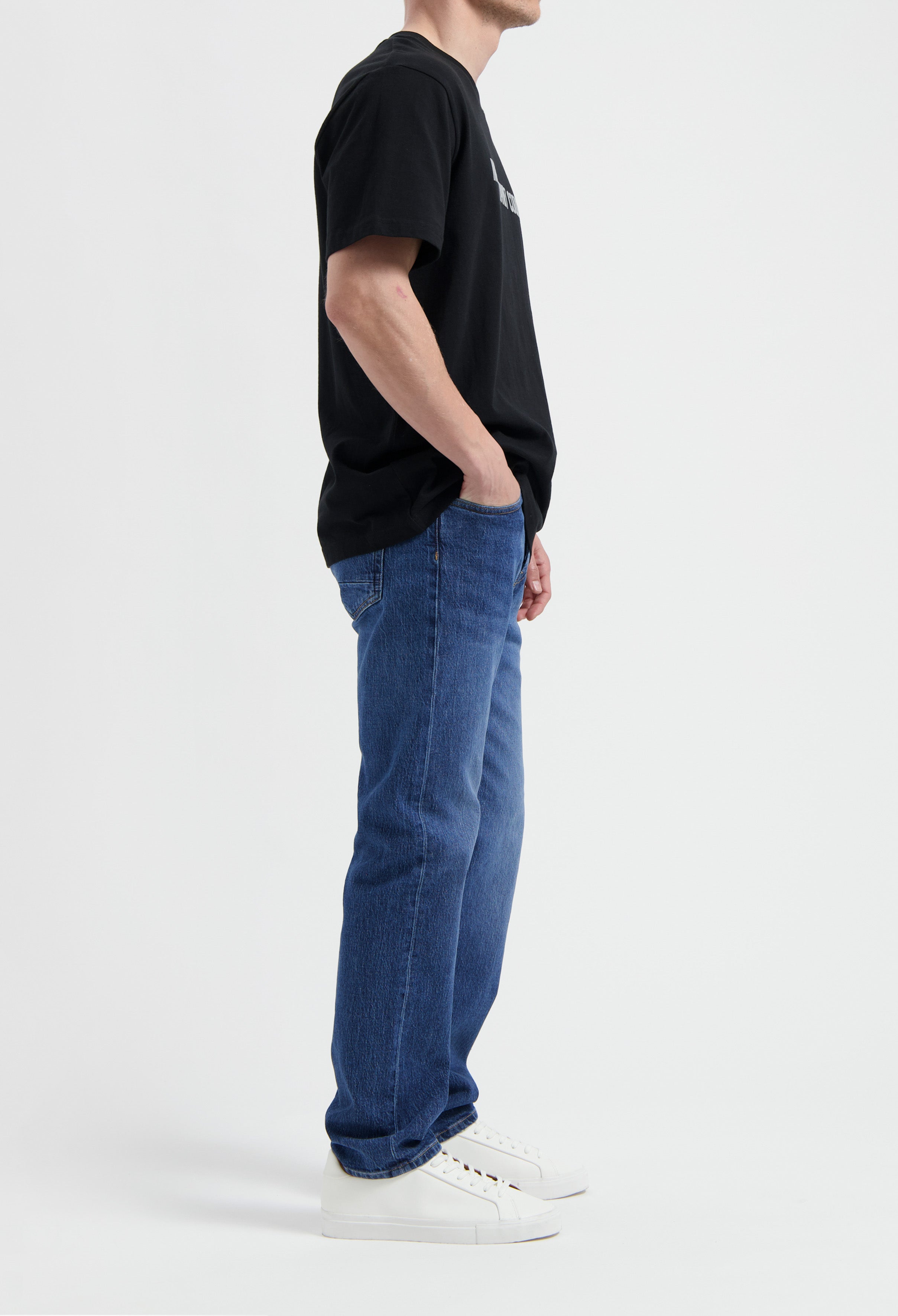 Sustainable MUD Jeans in dark denim, crafted from organic cotton, paired with a white tee and ethical white sneakers.