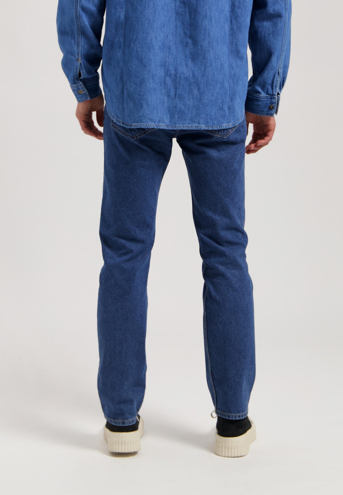 Sustainable MUD Jeans in dark denim, crafted ethically from organic cotton, shown with a white shirt and black shoes.