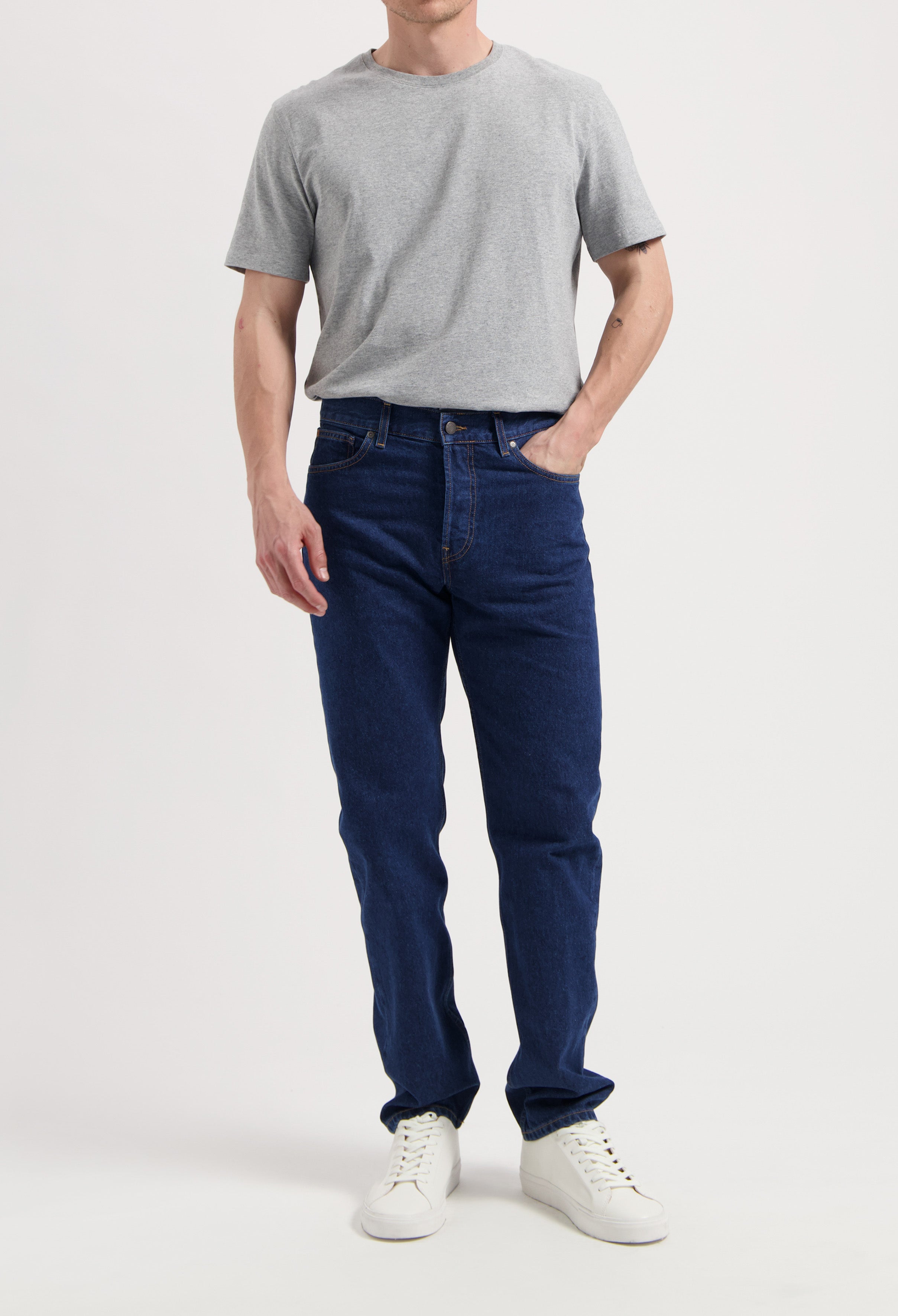 Sustainable MUD Jeans in dark denim, paired with a white T-shirt and brown sweater, showcasing ethical fashion.