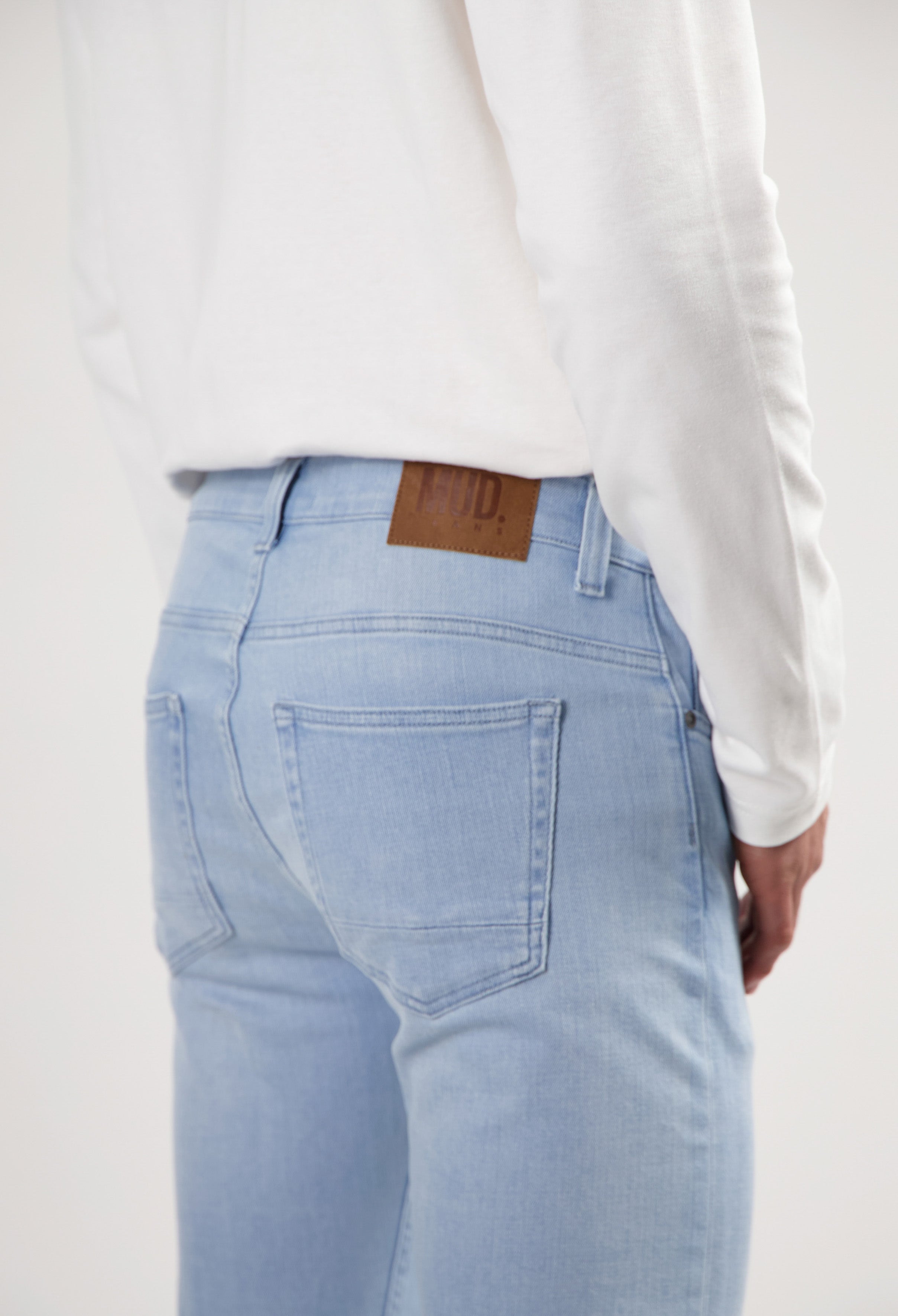 Sustainable MUD Jeans in dark denim, crafted from organic cotton, styled with black shoes and gray sweater.