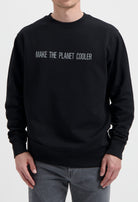 Sustainable MUD Jeans black sweater with "Make the Planet Cooler" slogan, paired with gray denim, ethical fashion choice.