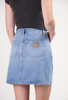 Light blue denim skirt by MUD Jeans, high-waisted with back pockets, paired with a black cropped top, showcasing casual style.