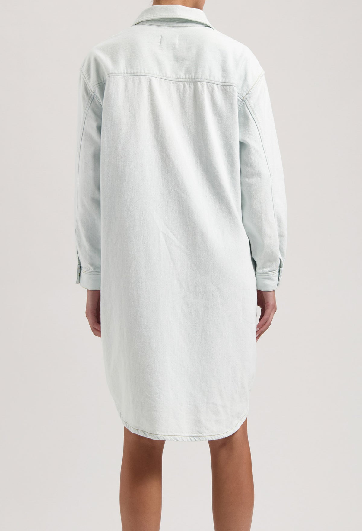 Back view of a light blue denim shirt dress showing a relaxed fit with long sleeves and classic collar design.