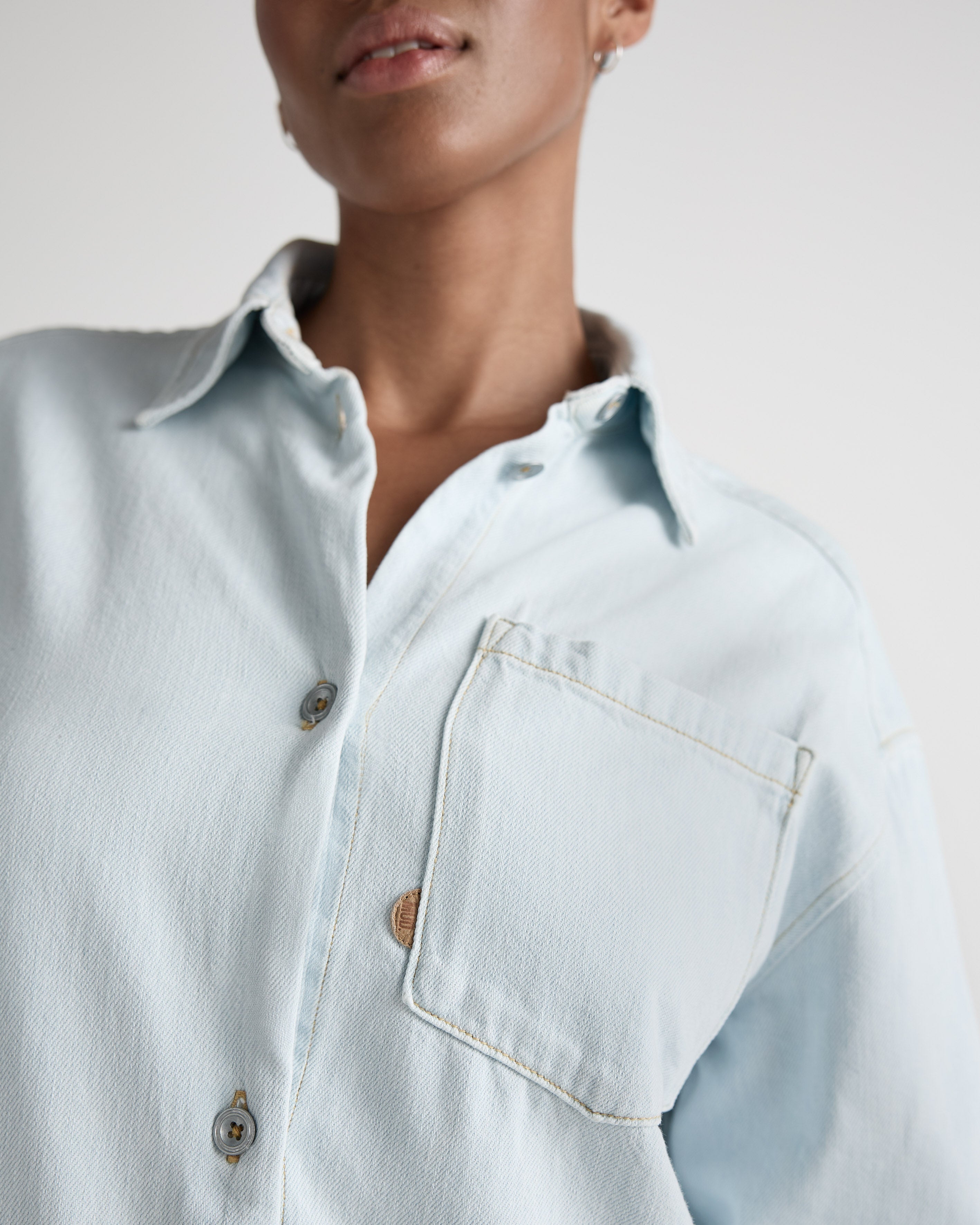 Close-up of a light blue denim shirt with button-up front and chest pocket, showcasing casual fashion style.