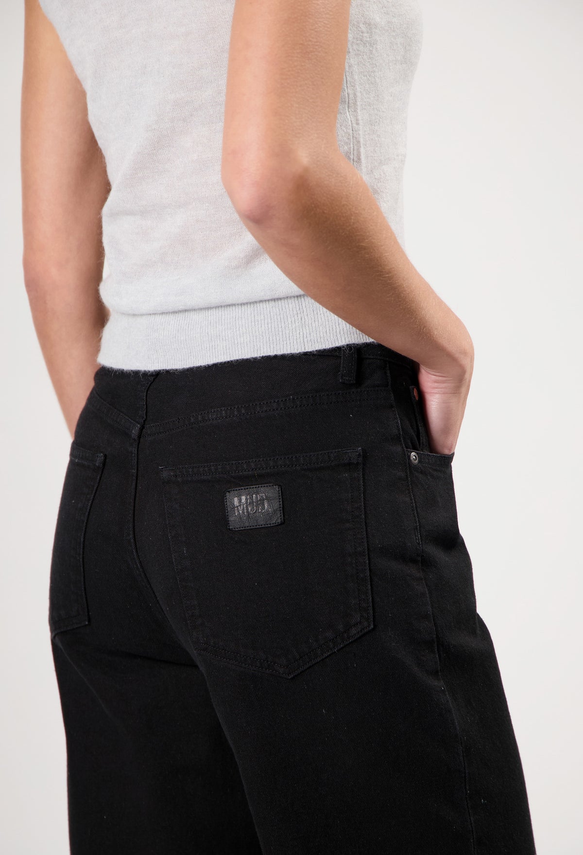 Model wearing black MUD Jeans made from organic cotton, featuring a light gray sleeveless top for an eco-friendly fashion look.