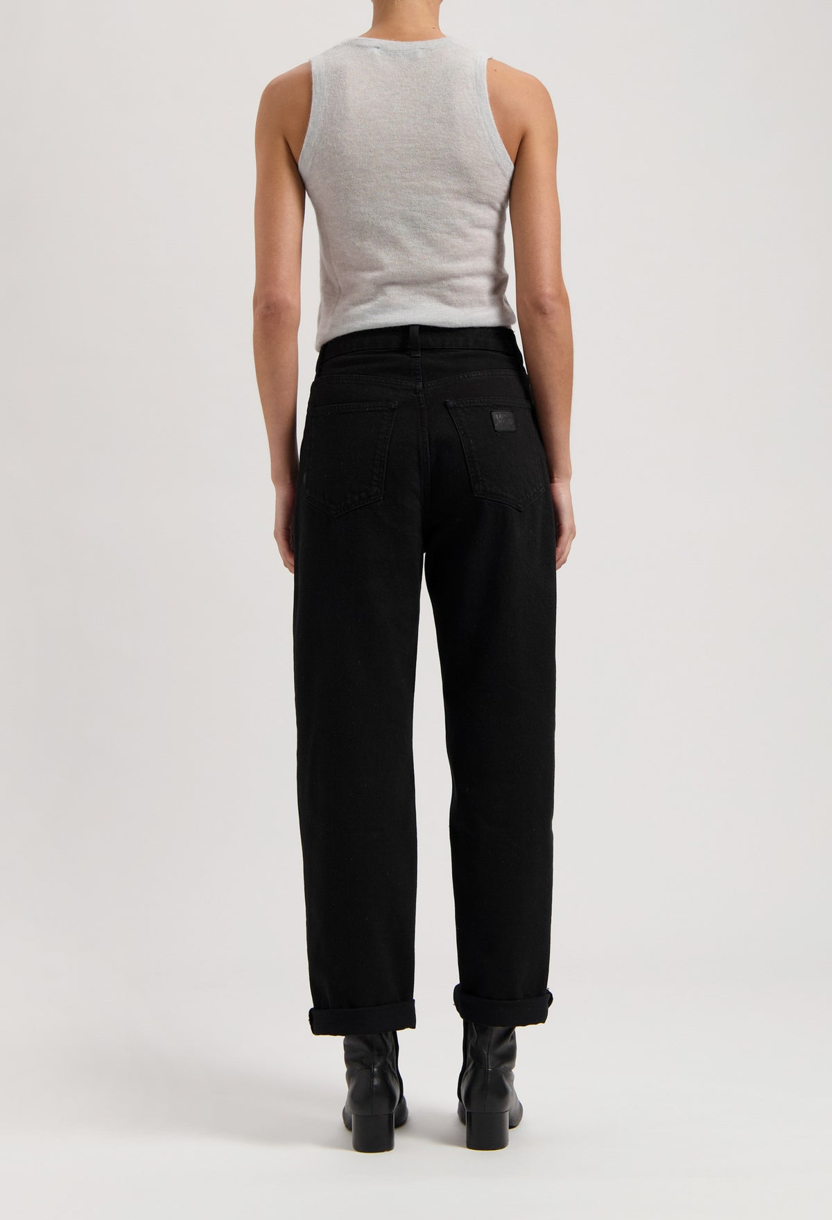 Back view of model wearing black high-waisted jeans paired with a gray sleeveless top, showcasing modern casual fashion style.