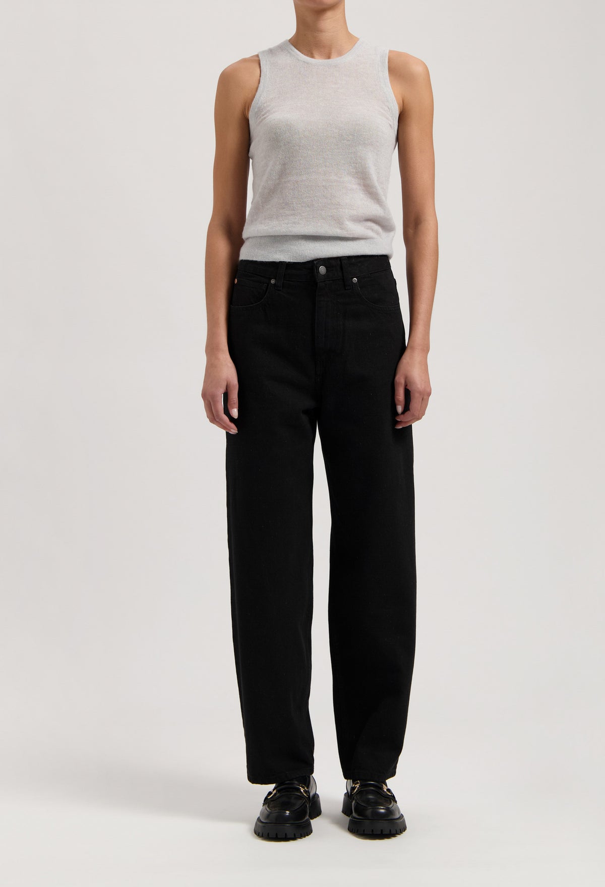 Model wearing a light gray sleeveless top and high-waisted black wide-leg jeans, paired with black shoes, against a plain background.