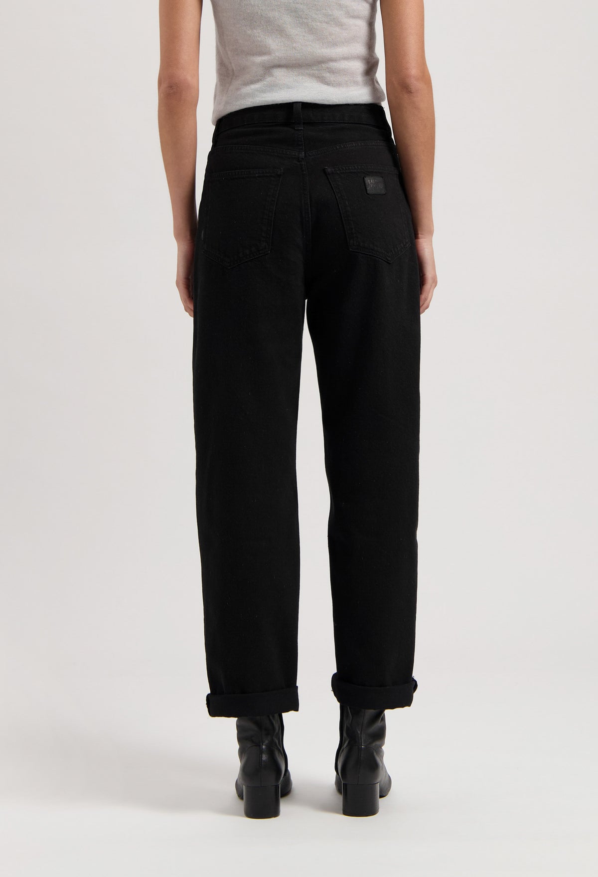 Black high-waisted jeans made of cotton, shown from the back, paired with black boots and a light gray sleeveless top.