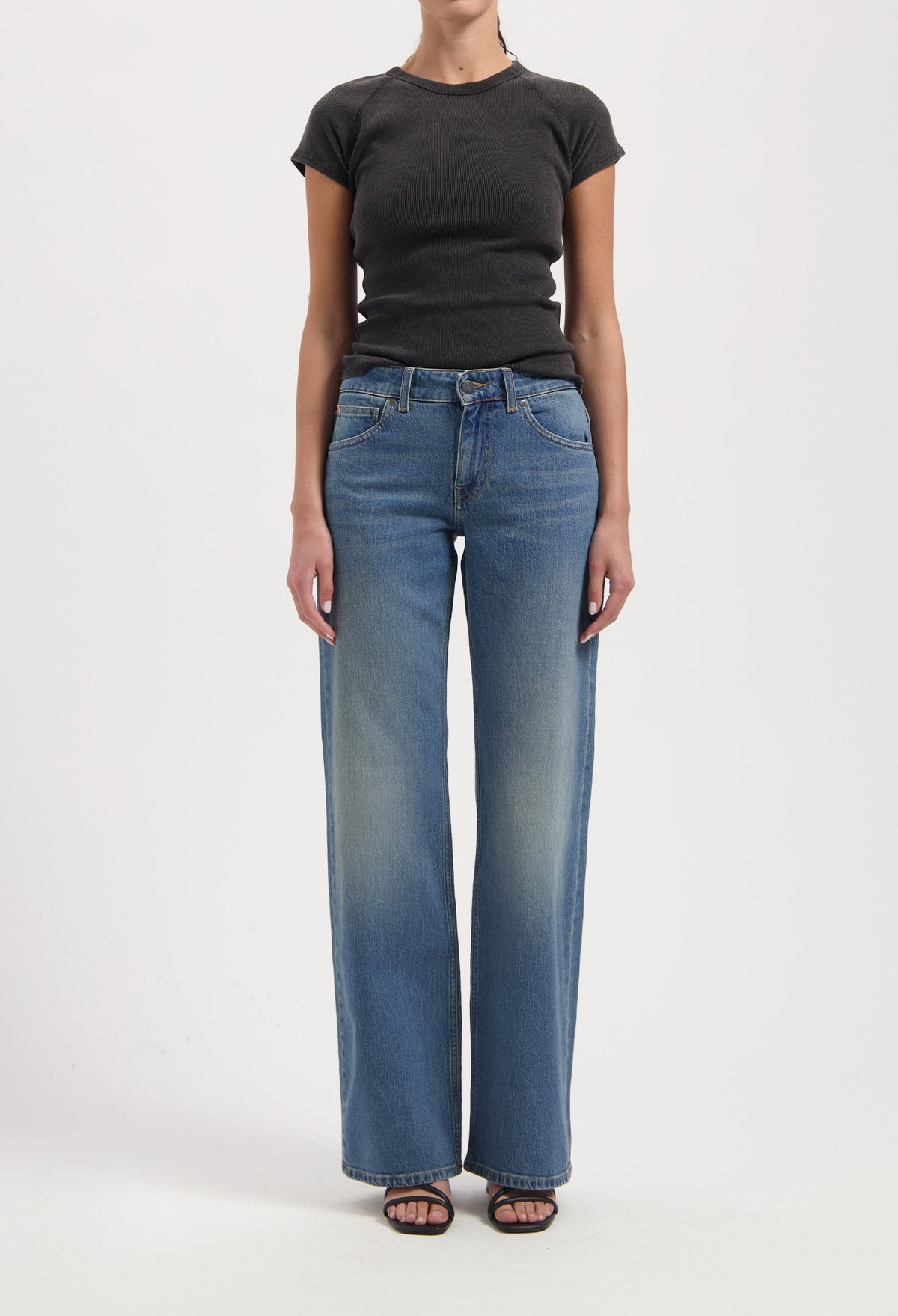 Wide-leg blue jeans with faded effect, paired with a fitted black short-sleeve top, worn by a model against a plain background.