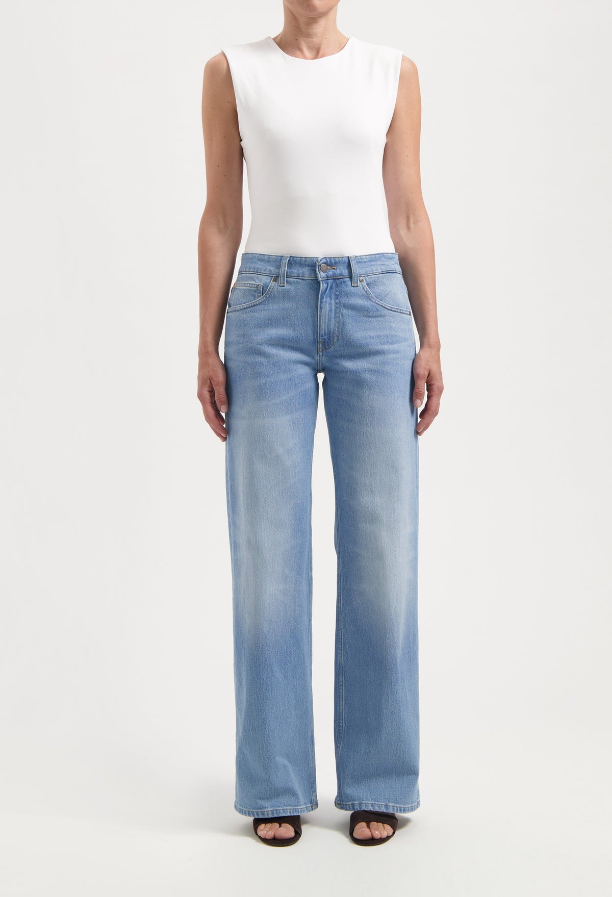 Light blue, high-waisted wide-leg jeans paired with a sleeveless white top worn by a woman standing against a plain backdrop.