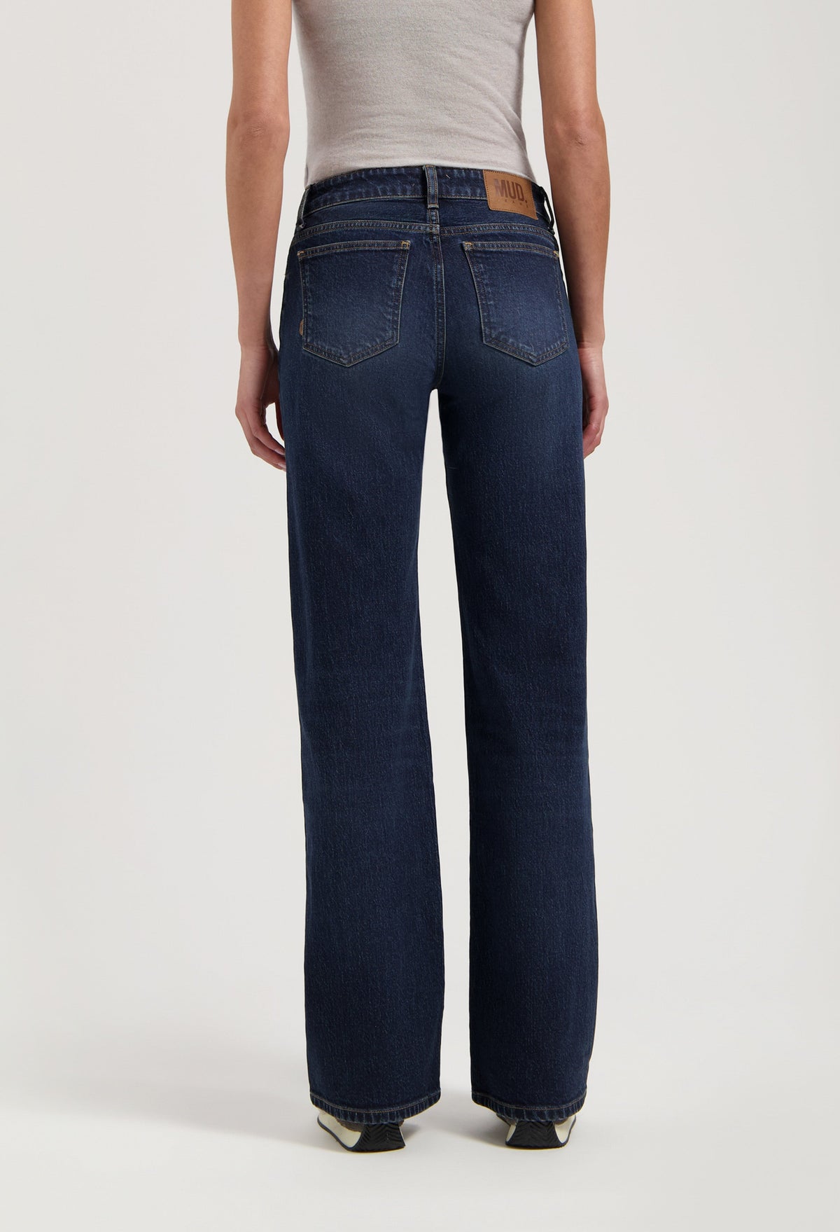 Back view of dark blue sustainable jeans from MUD Jeans, featuring a wide-leg style, paired with a fitted beige tank top.