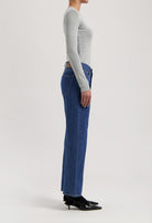 Side view of woman wearing high-waisted blue denim jeans and a light gray long-sleeve top, paired with black heels.