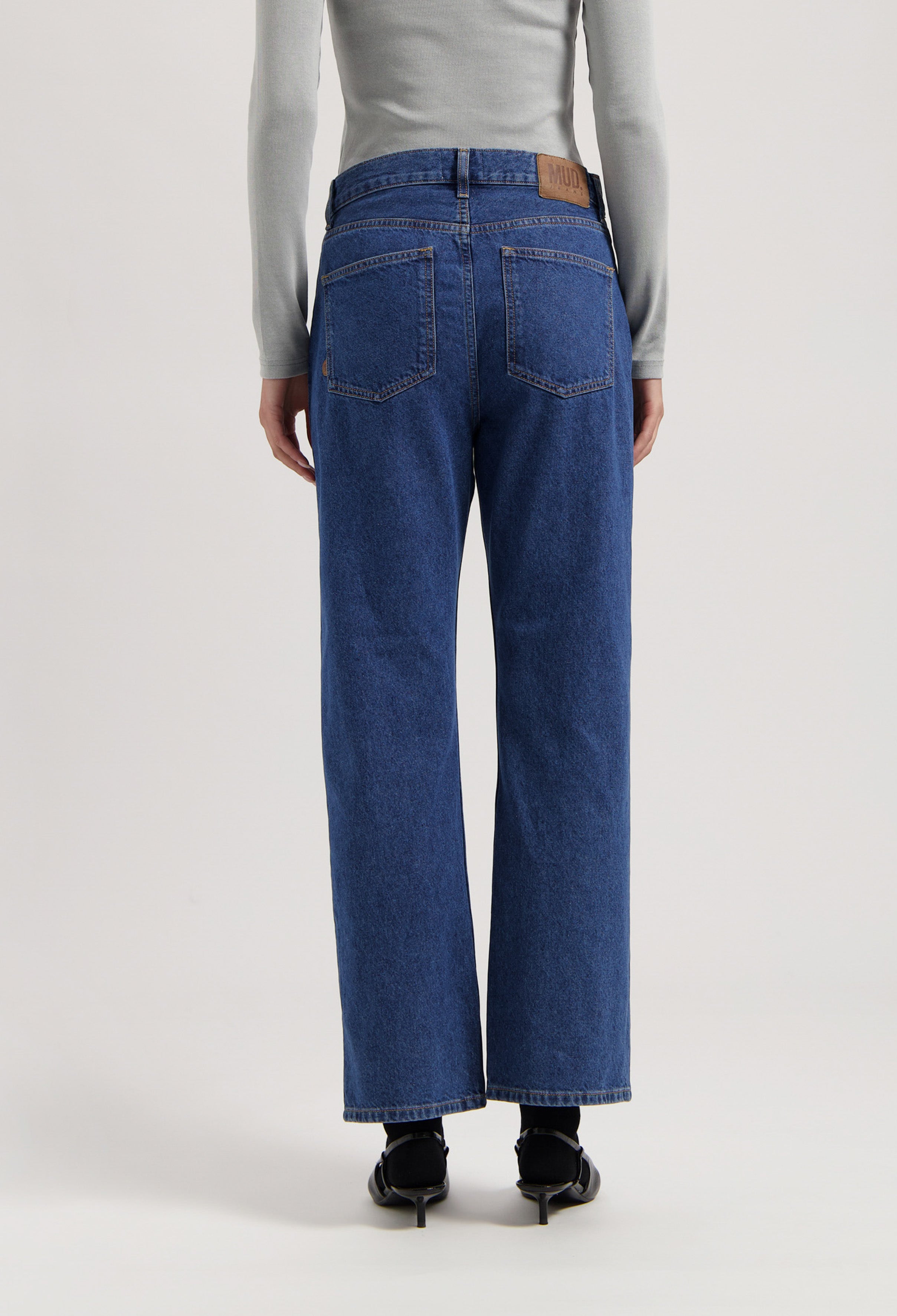 Back view of sustainable MUD Jeans, organic blue denim, wide-leg fit, paired with a light gray long-sleeve top.