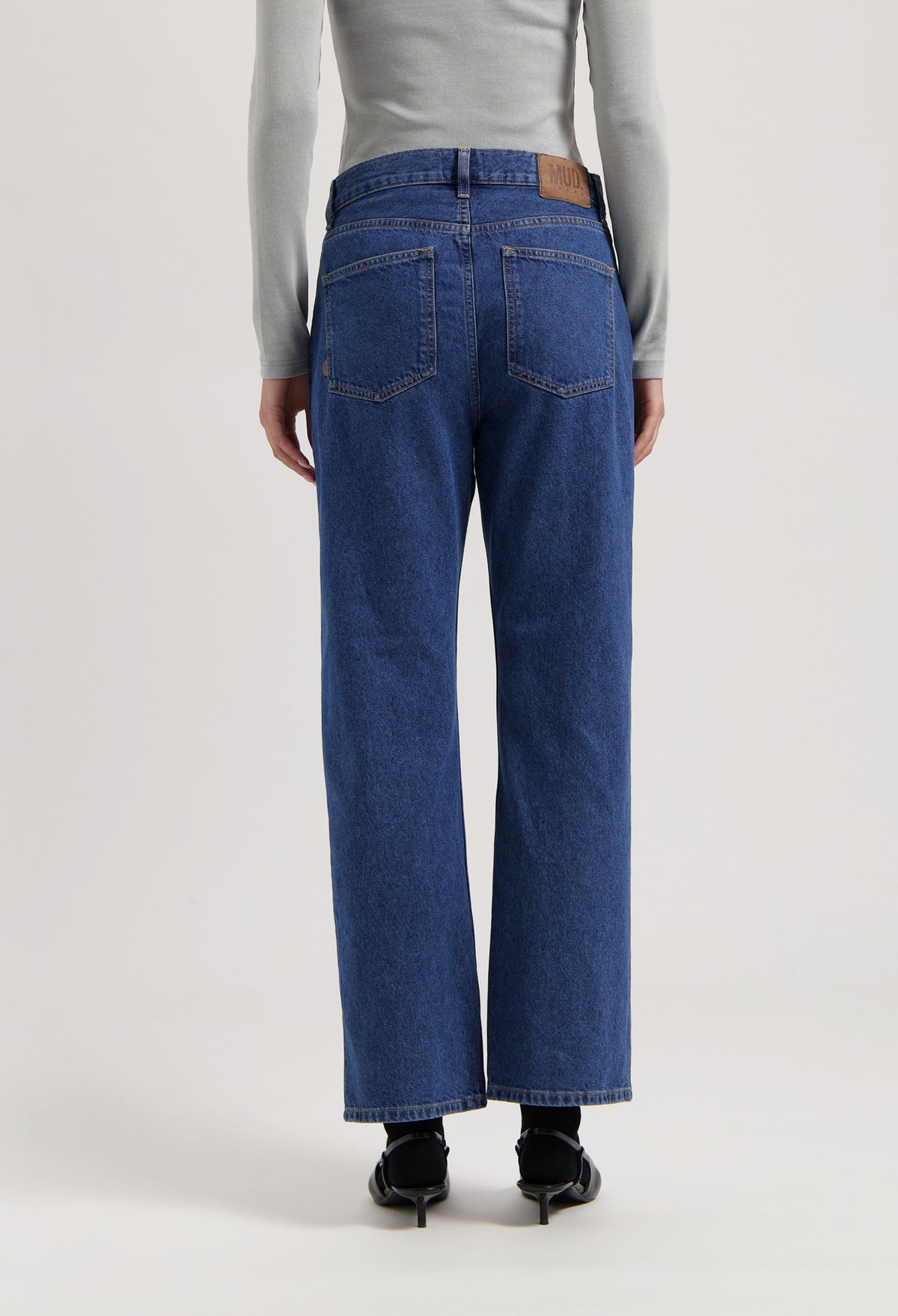 Back view of sustainable MUD Jeans, organic blue denim, wide-leg fit, paired with a light gray long-sleeve top.