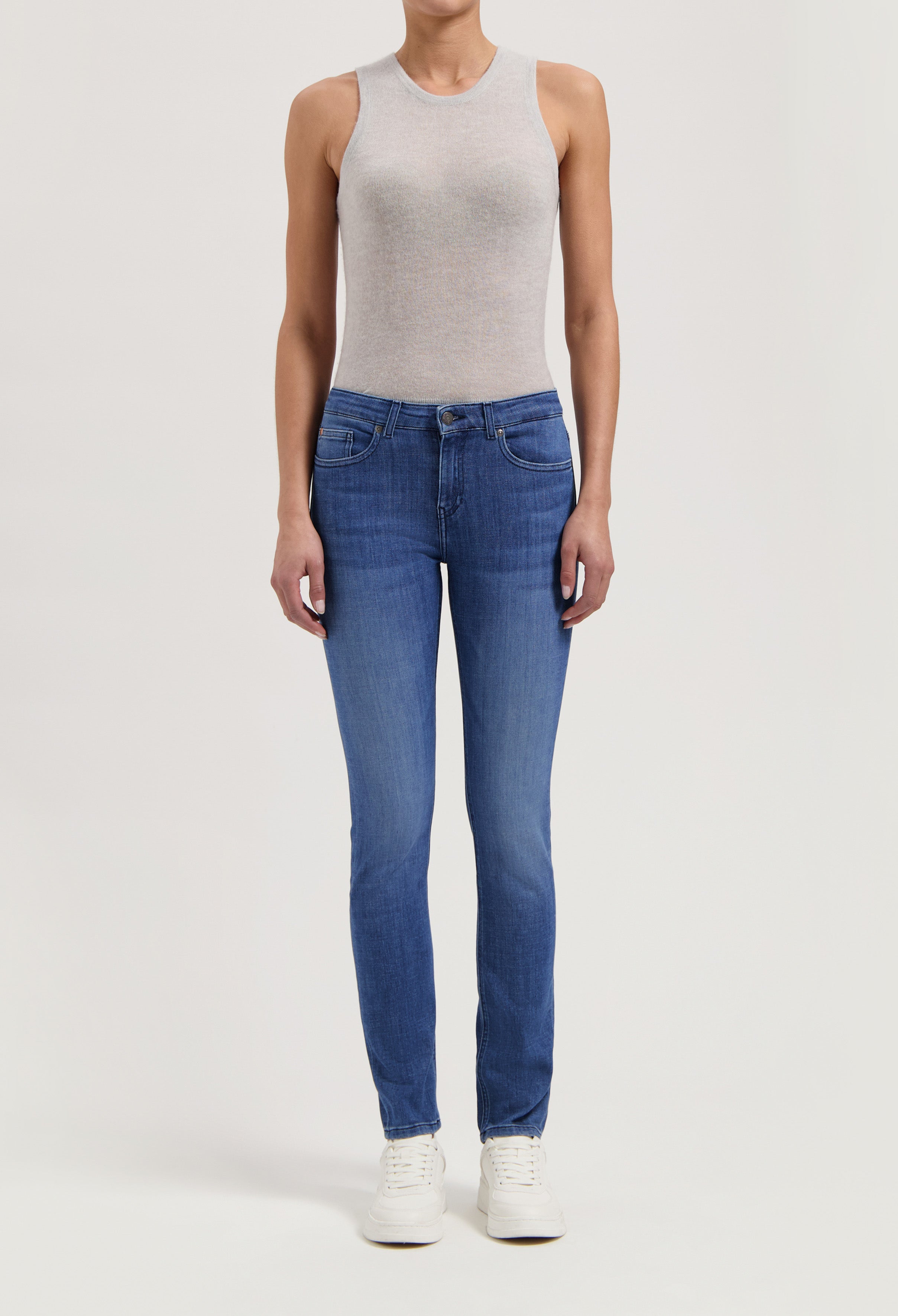 Sleeveless gray top with slim-fit blue denim jeans and white sneakers, showcasing a casual and modern style.