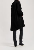 Long black shirt dress styled over dark denim jeans and black pointed-toe heels, showcasing a minimalist fashion look.