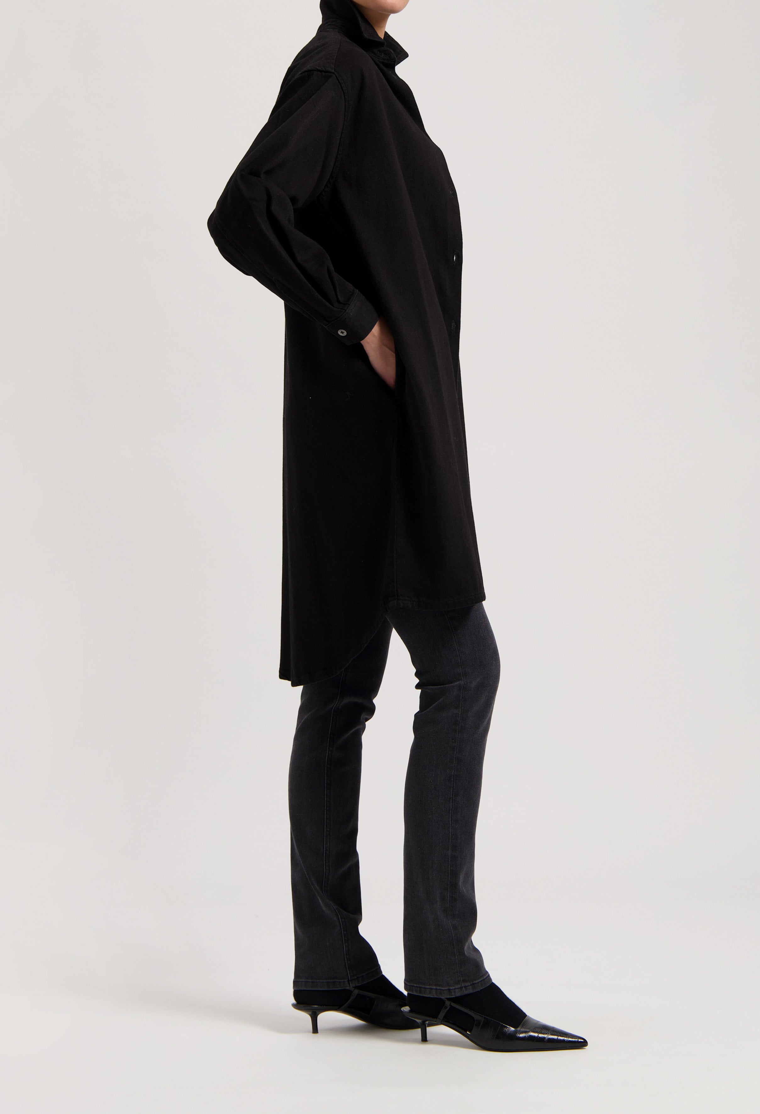 Black oversized shirt dress paired with dark gray, straight-leg jeans and pointed black kitten heels.