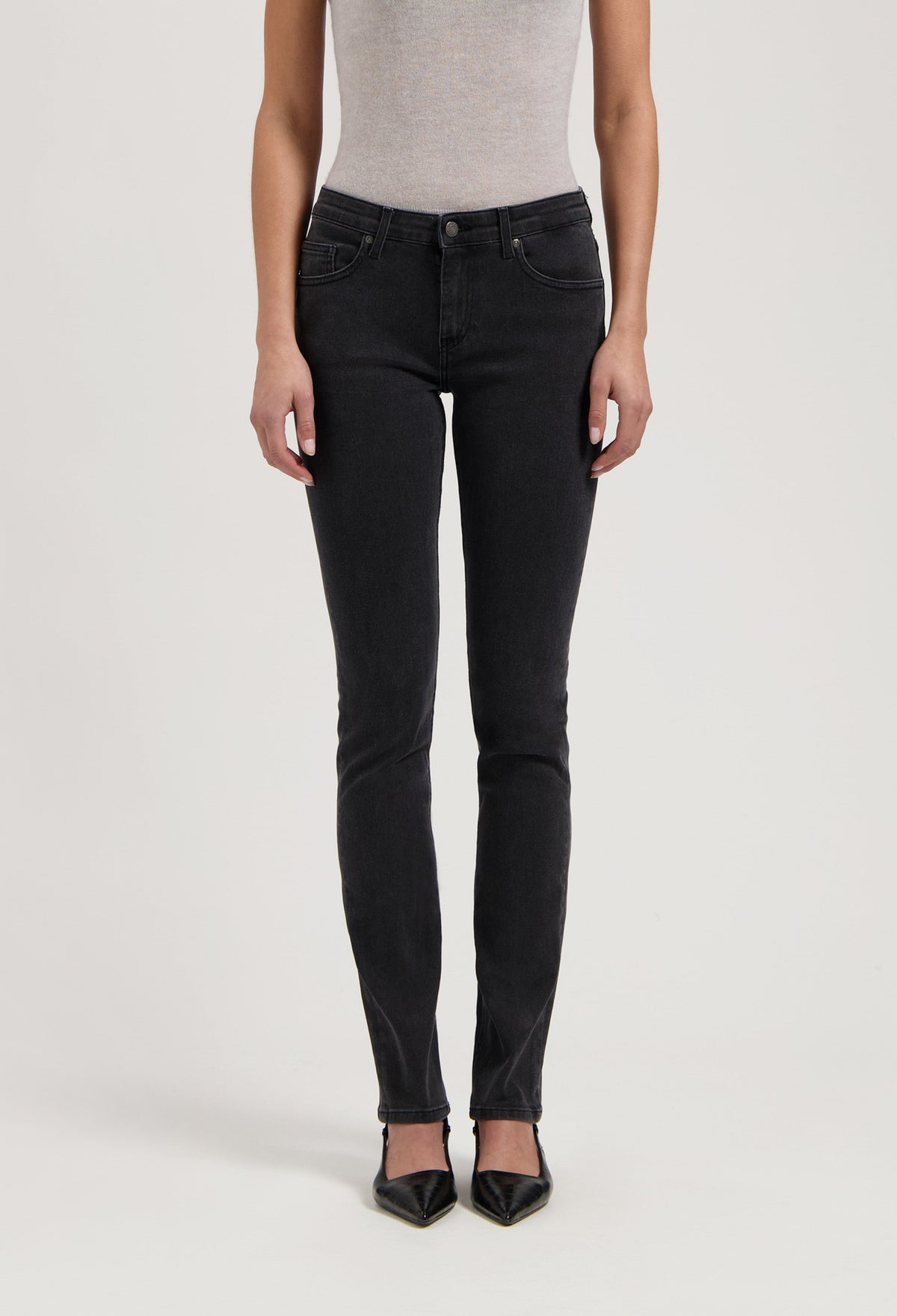 Woman wearing fitted black denim jeans paired with a light gray sleeveless top and pointed black shoes.