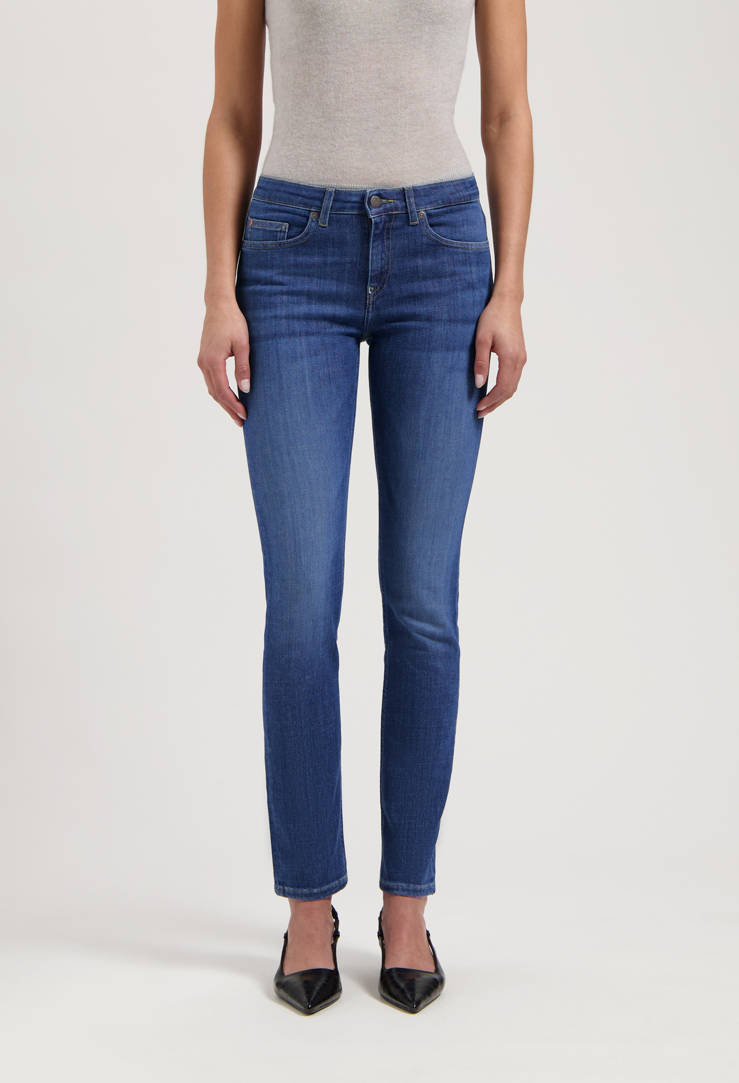 Woman wearing blue slim-fit jeans with a light gray sleeveless top, paired with black pointed heels.