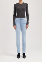 Slim-fit light blue denim jeans with a button closure, paired with a charcoal gray long-sleeve top, modeled standing.
