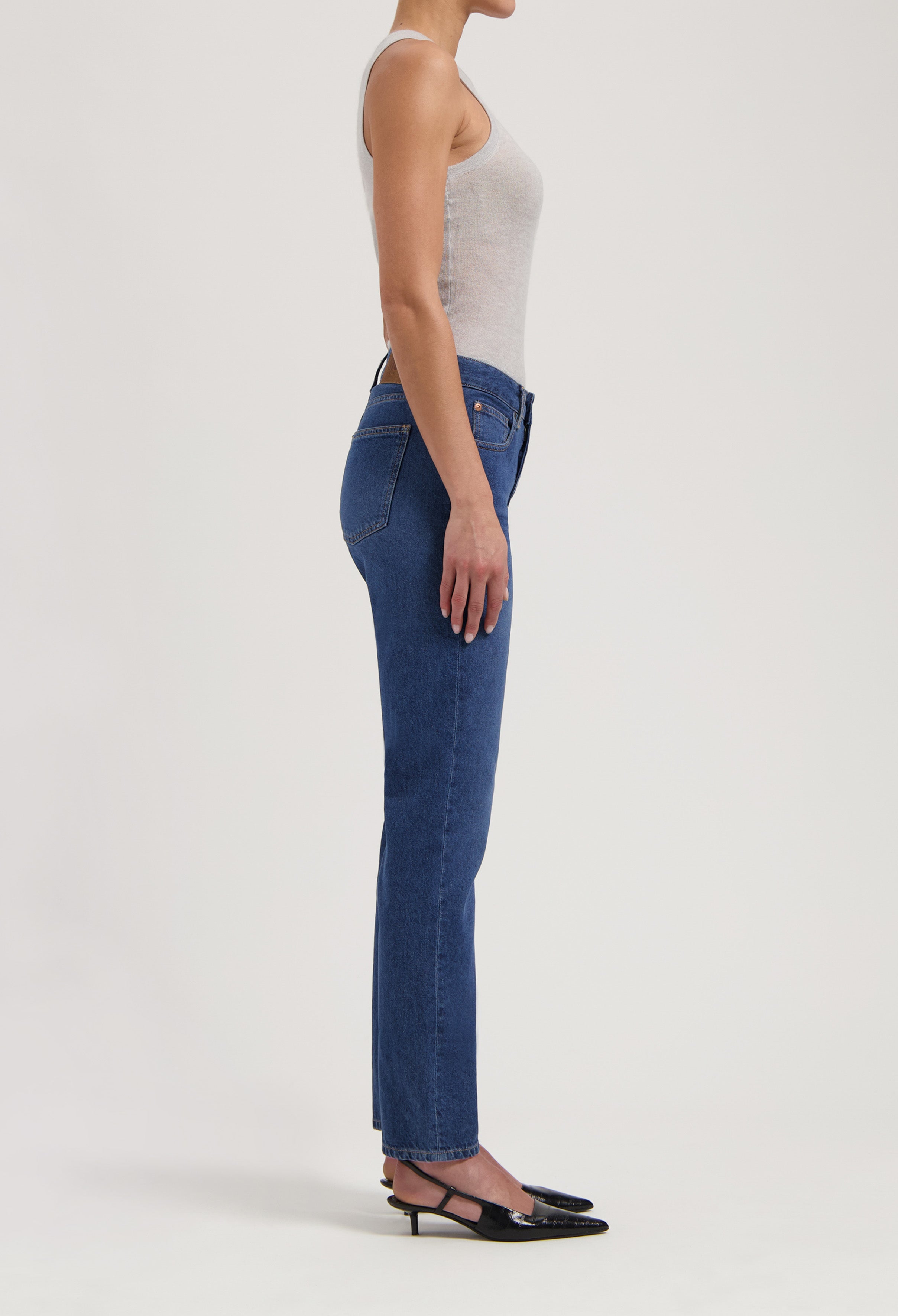 Side view of a person wearing blue denim jeans and a light gray sleeveless top paired with black slingback heels.