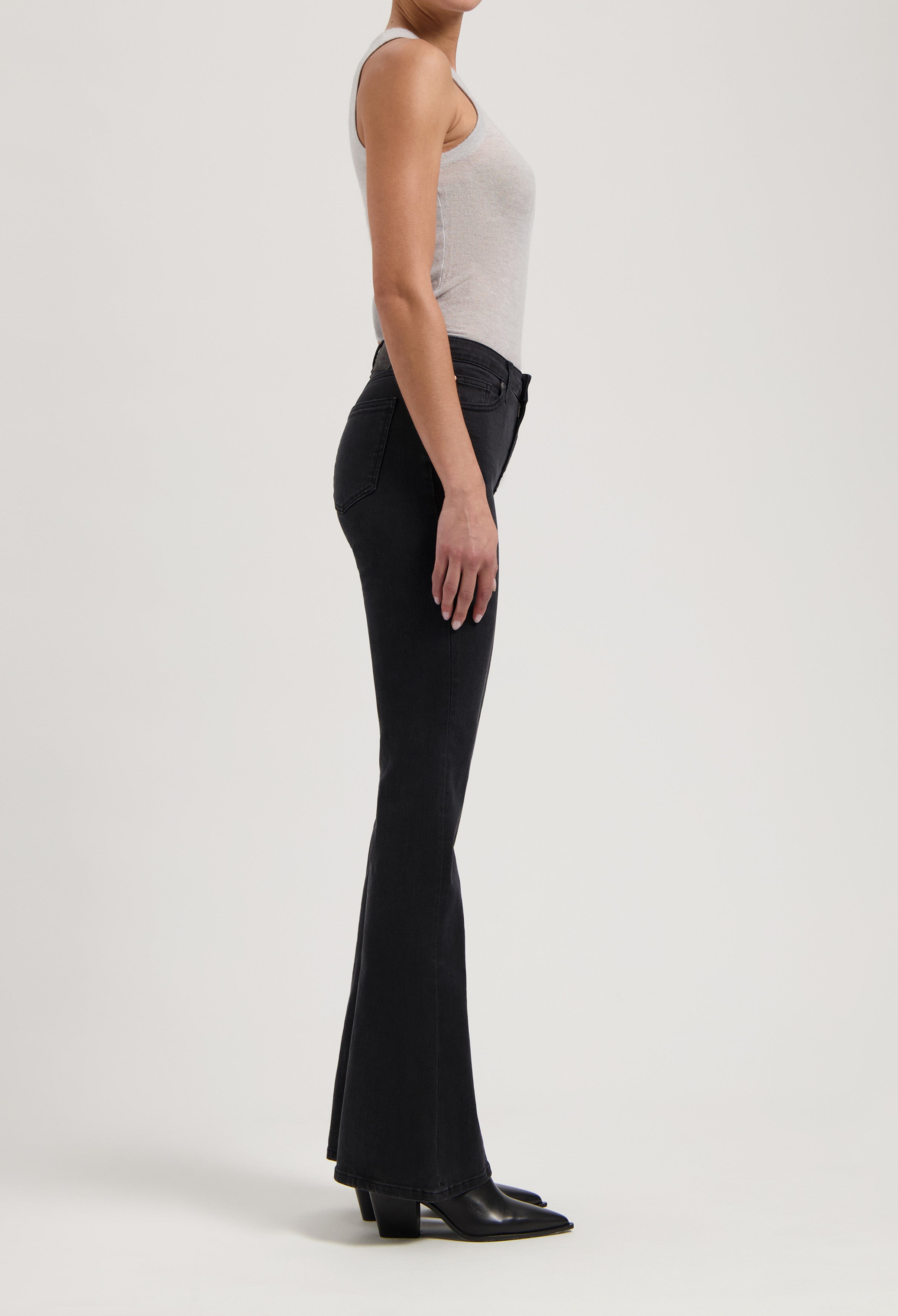 Side profile of a person wearing slim-fit black flared jeans paired with a casual light gray tank top and black boots.