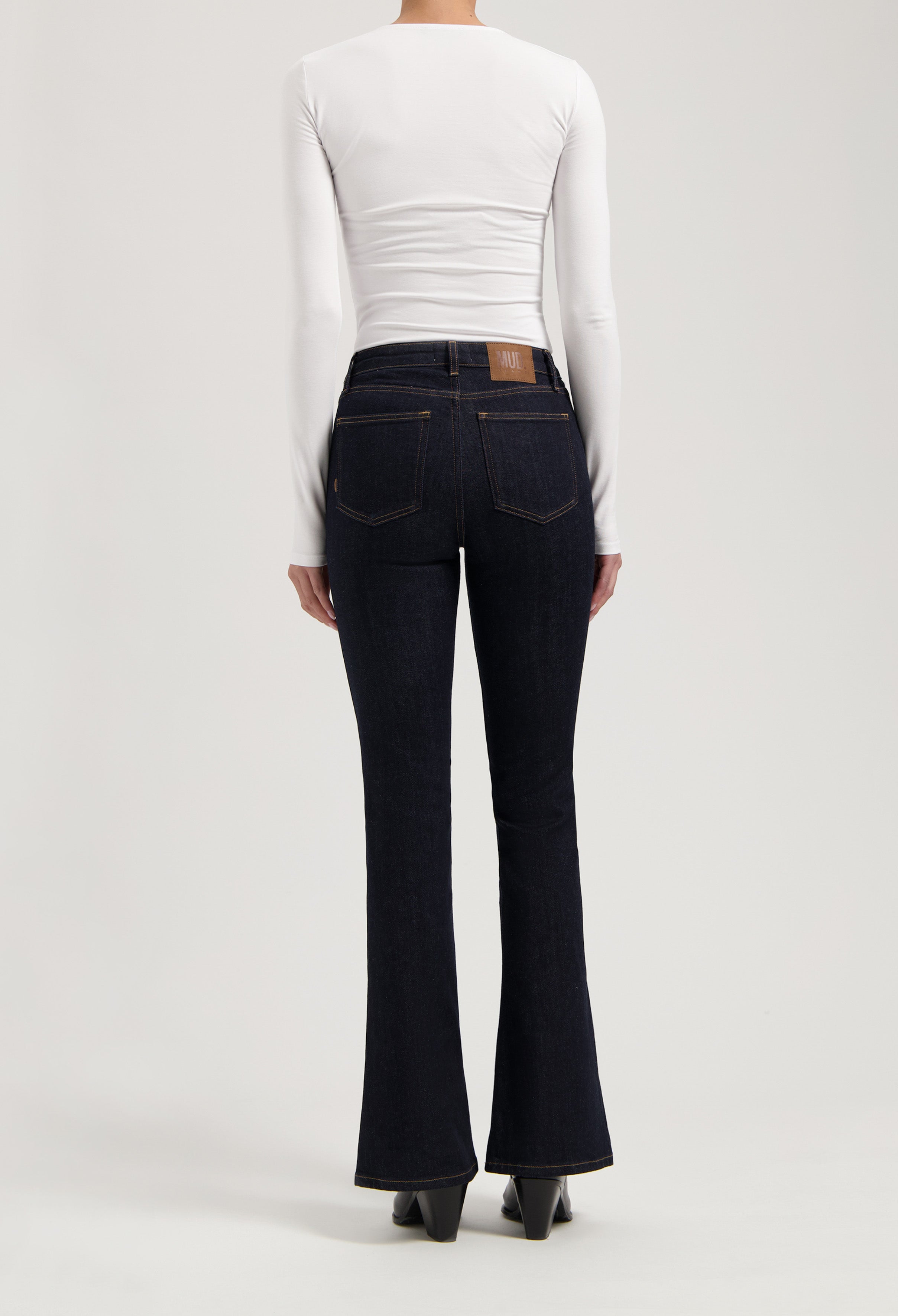 Dark blue flared denim jeans paired with a form-fitting white long sleeve top, highlighting a modern casual style.