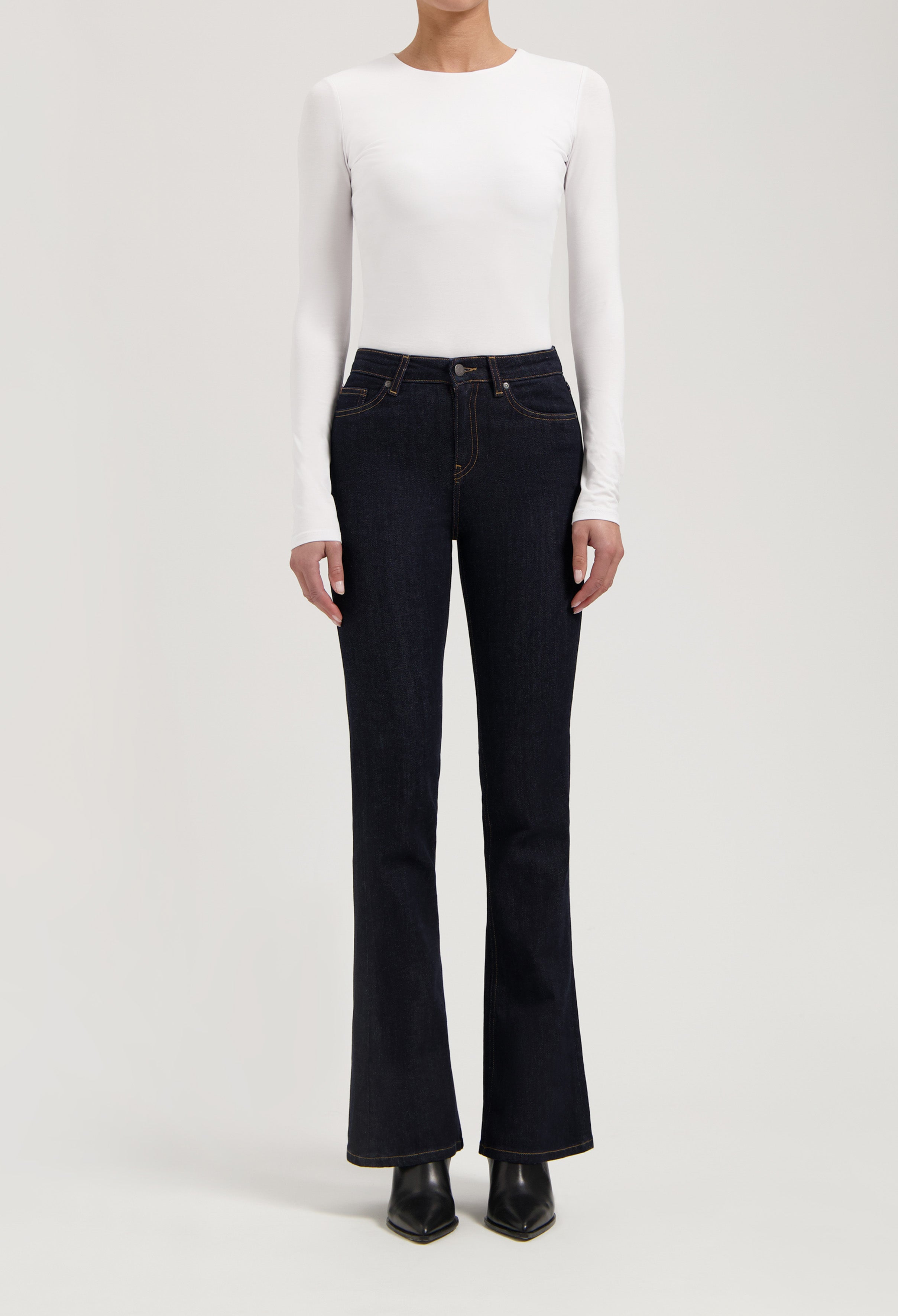 Woman wearing dark blue bootcut jeans with a white long-sleeve fitted top, showcasing casual chic style.