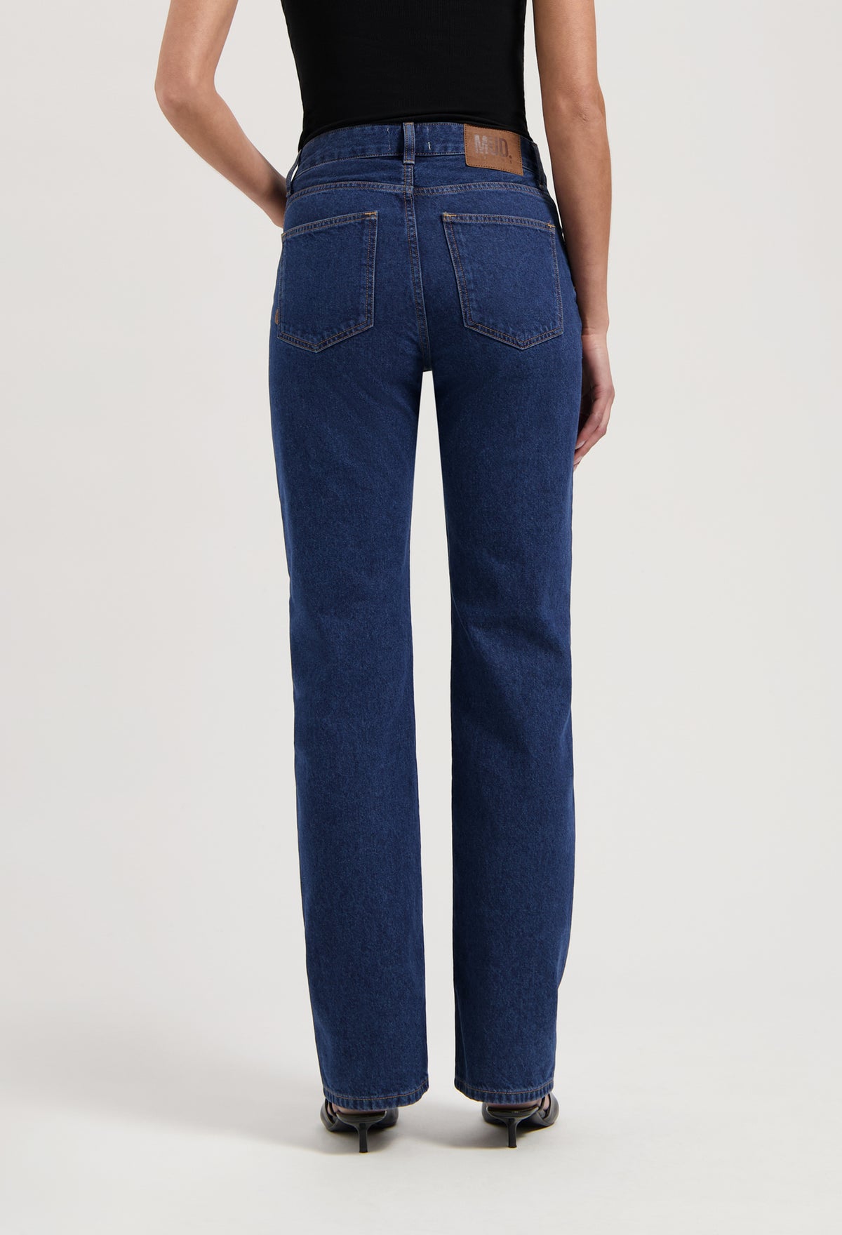 High-waisted, eco-friendly deep blue women's jeans showcasing straight-leg fit, paired with a black sleeveless top.