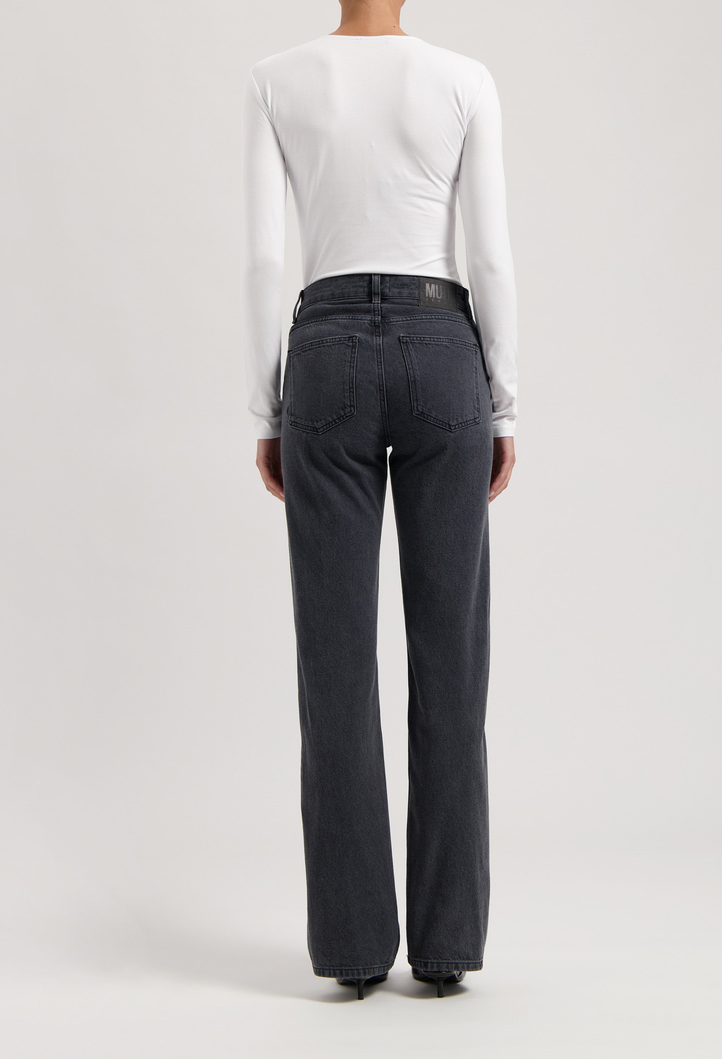 Person wearing dark gray straight-leg jeans with a high waist, paired with a fitted long-sleeve white top, viewed from the back.