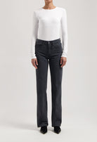 Model wearing high-waisted, black denim jeans paired with a white long-sleeve fitted top and black pointed shoes.