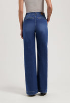 Wide-leg blue denim jeans worn with a sleeveless gray top, highlighting relaxed fit and mid-rise waist in a studio setting.