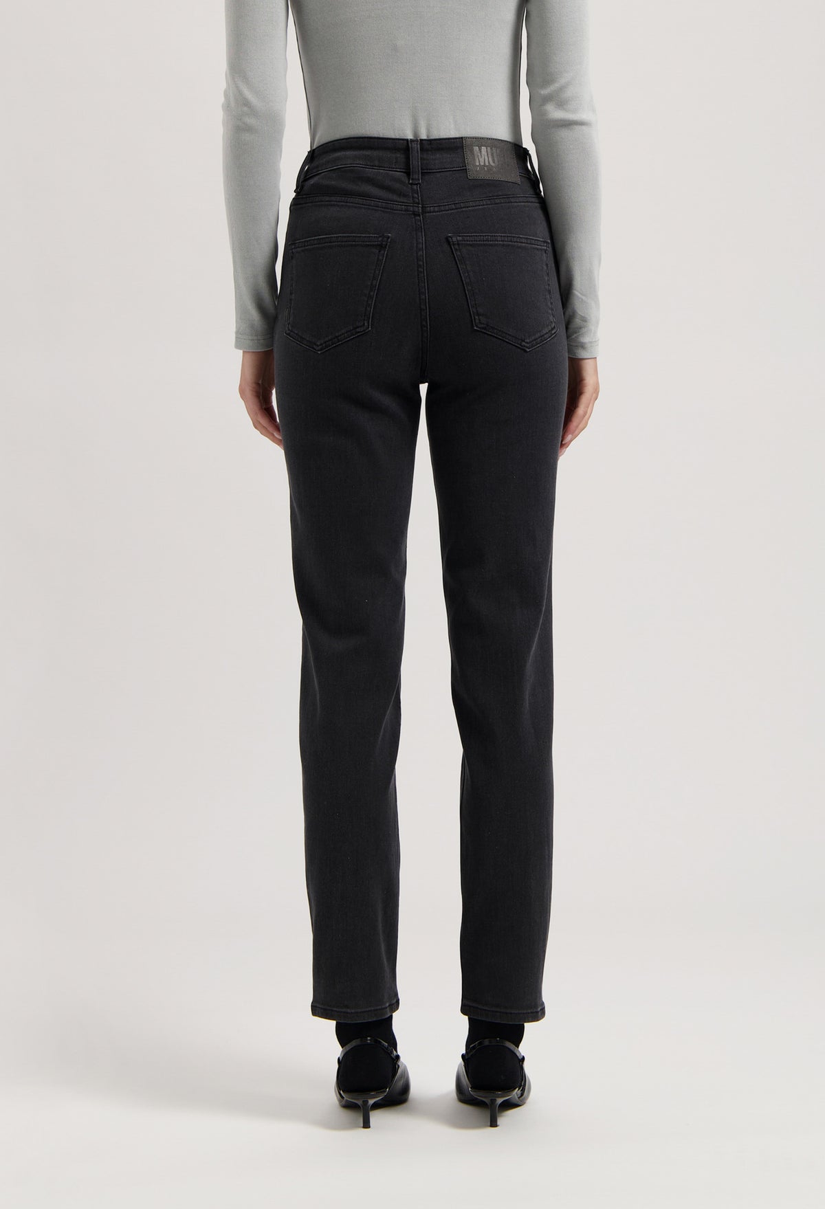 Back view of black, high-waisted denim jeans worn with a fitted gray long-sleeve top, showcasing modern casual fashion.