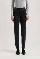 Person wearing black straight-leg jeans with a high-waist fit, paired with a light gray long-sleeve shirt and black heels.