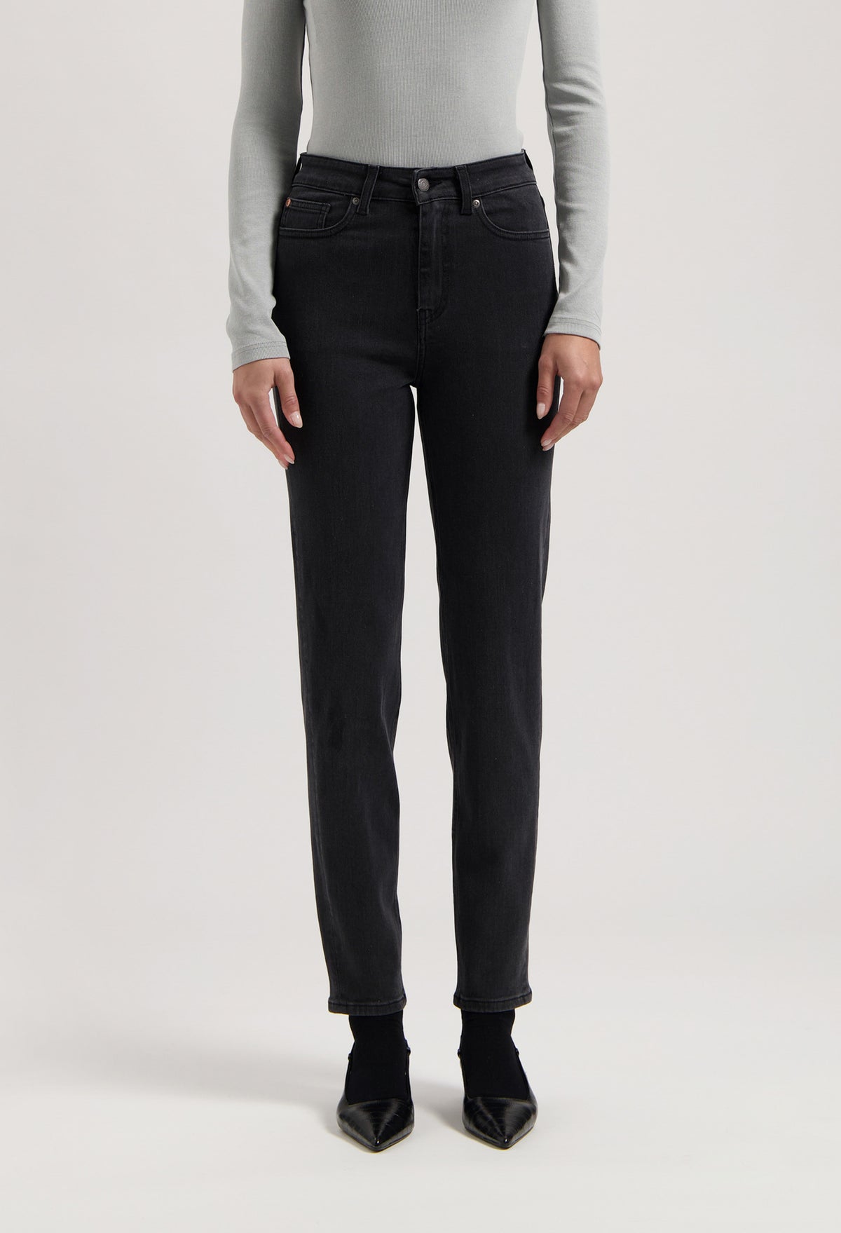 Person wearing black straight-leg jeans with a high-waist fit, paired with a light gray long-sleeve shirt and black heels.