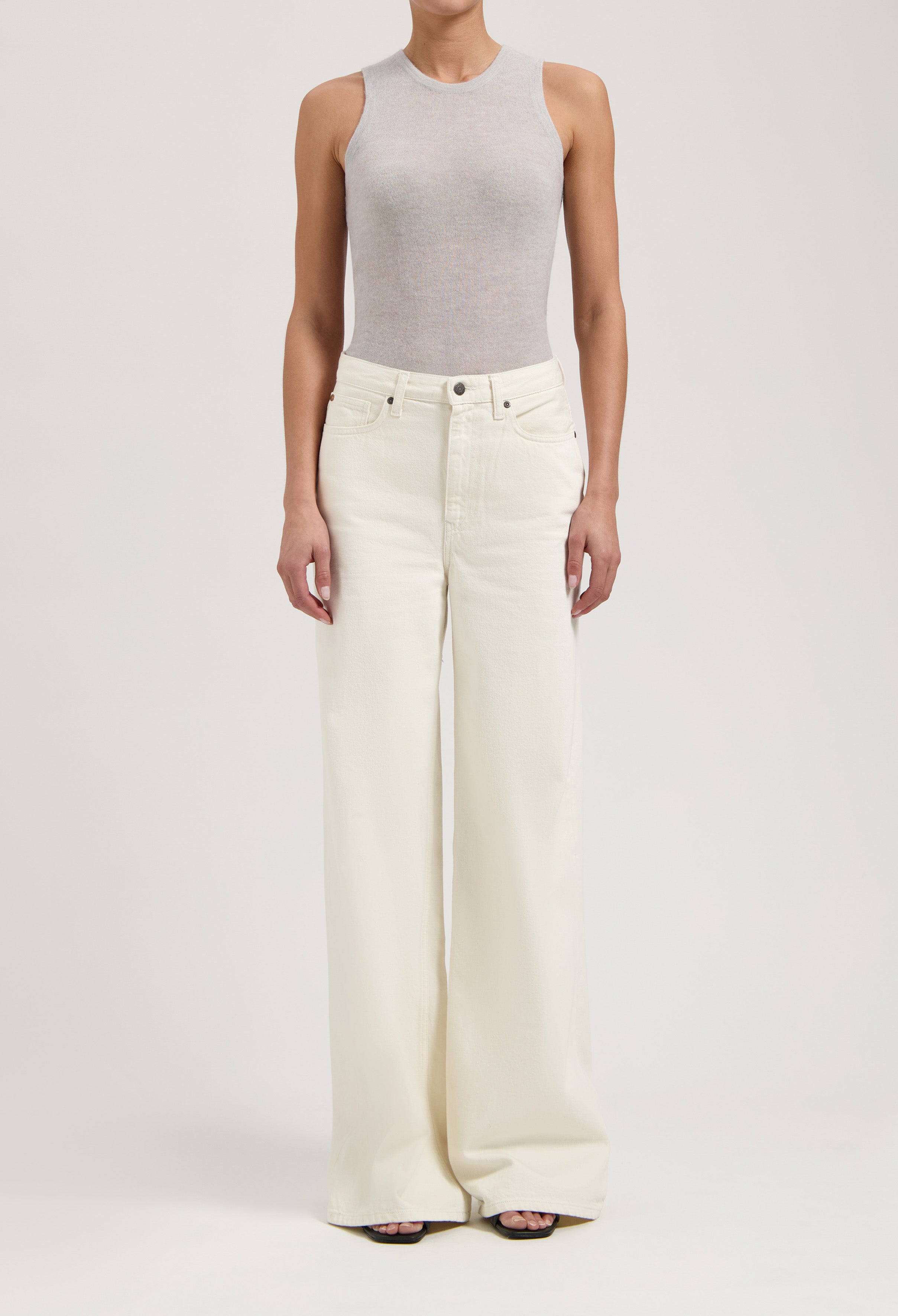 Woman wearing light gray sleeveless top paired with high-waisted, wide-leg white denim jeans, showcasing modern casual fashion.